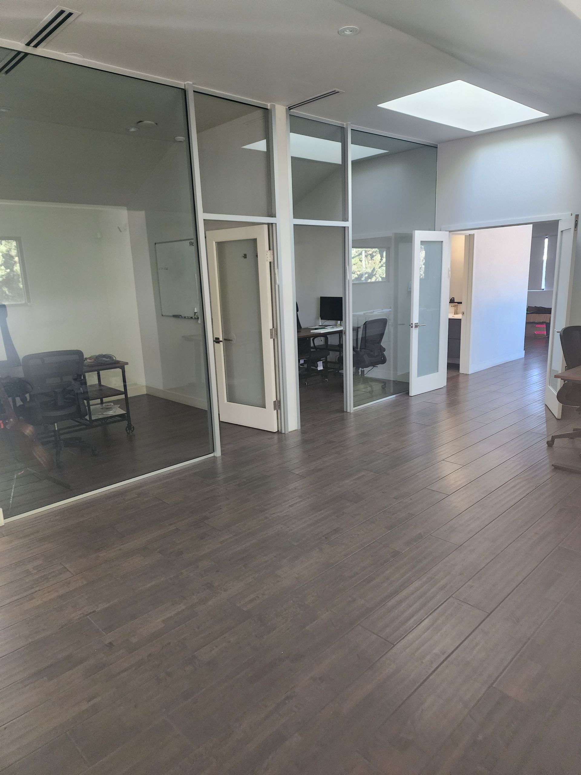 Empty modern office with glass-walled rooms, wood floors, and overhead lights