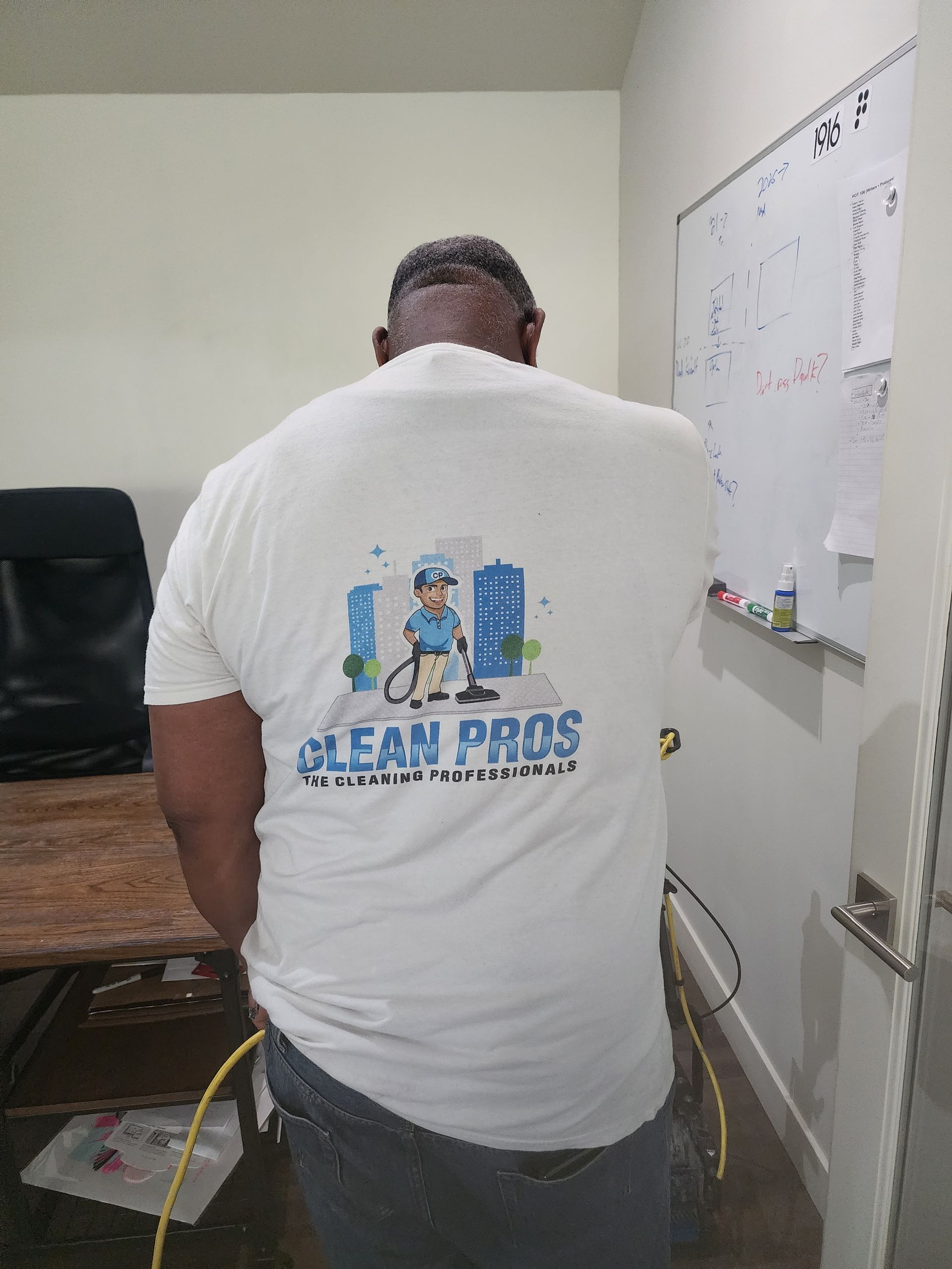 Person sitting at a desk in an office, wearing a white shirt with a logo on the back.