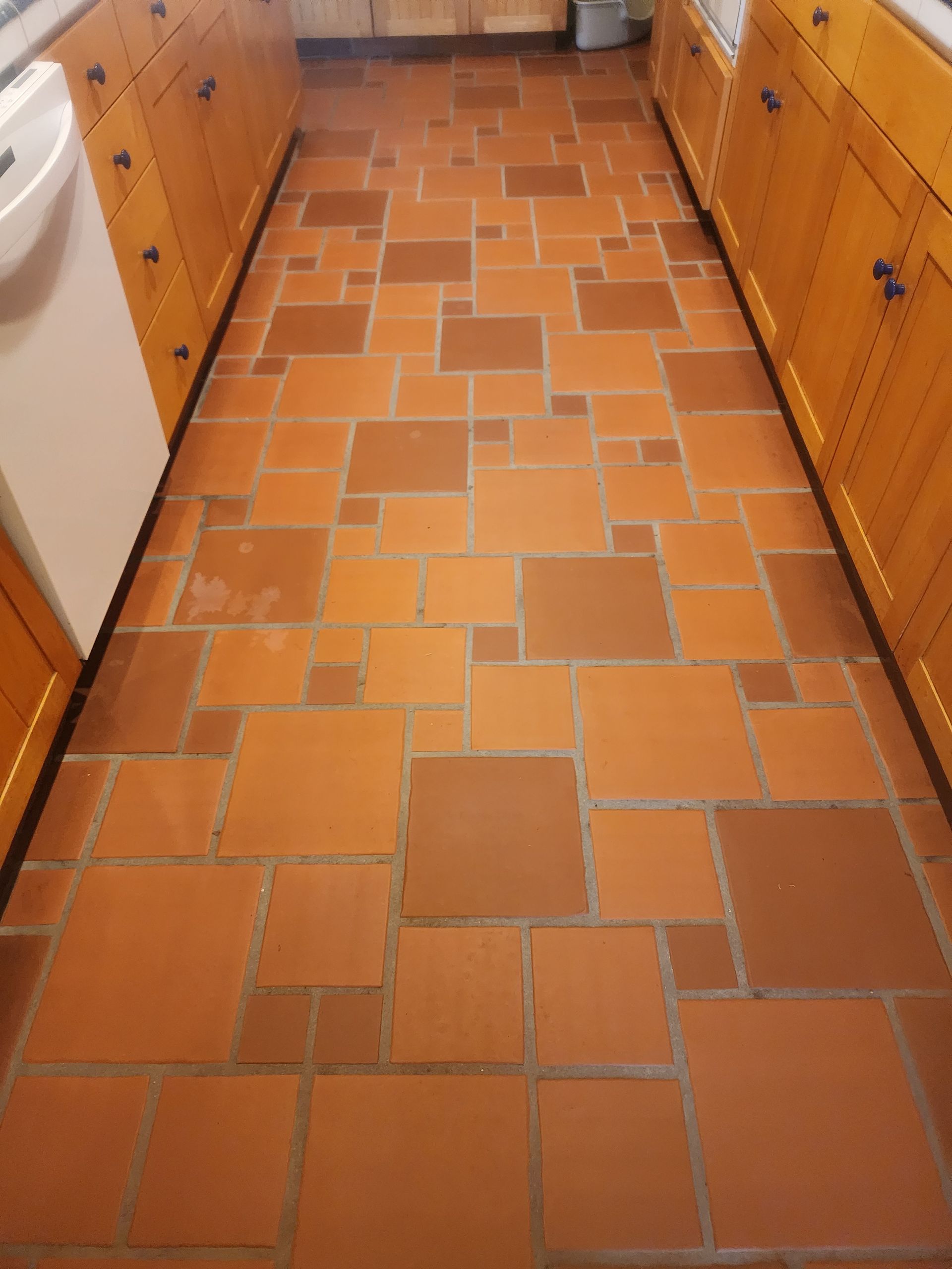 Narrow kitchen aisle with orange tile floor and wooden cabinets on both sides