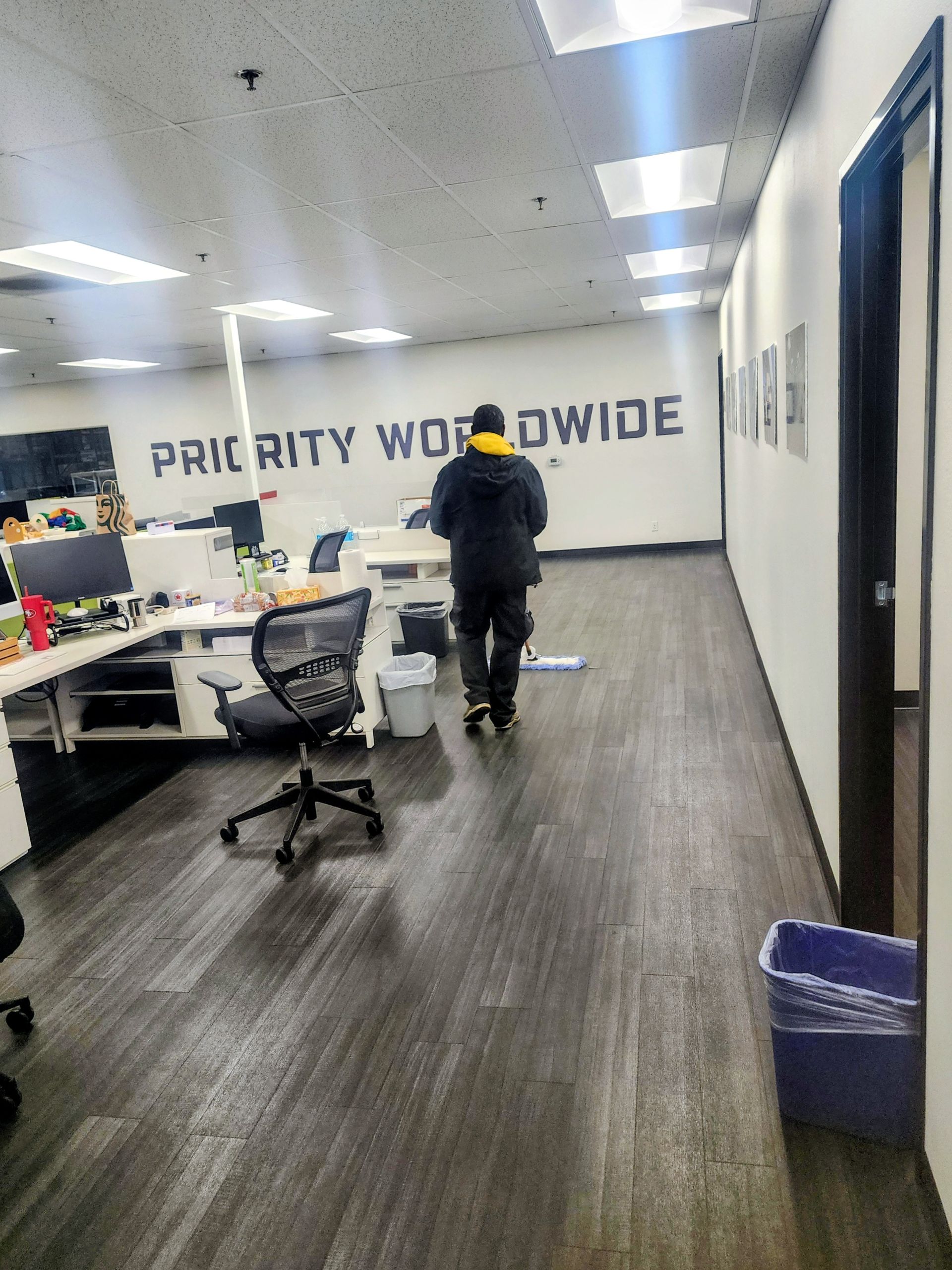 Office hallway with desks and a person walking toward a wall reading “PIRITY WORLDWIDE.”