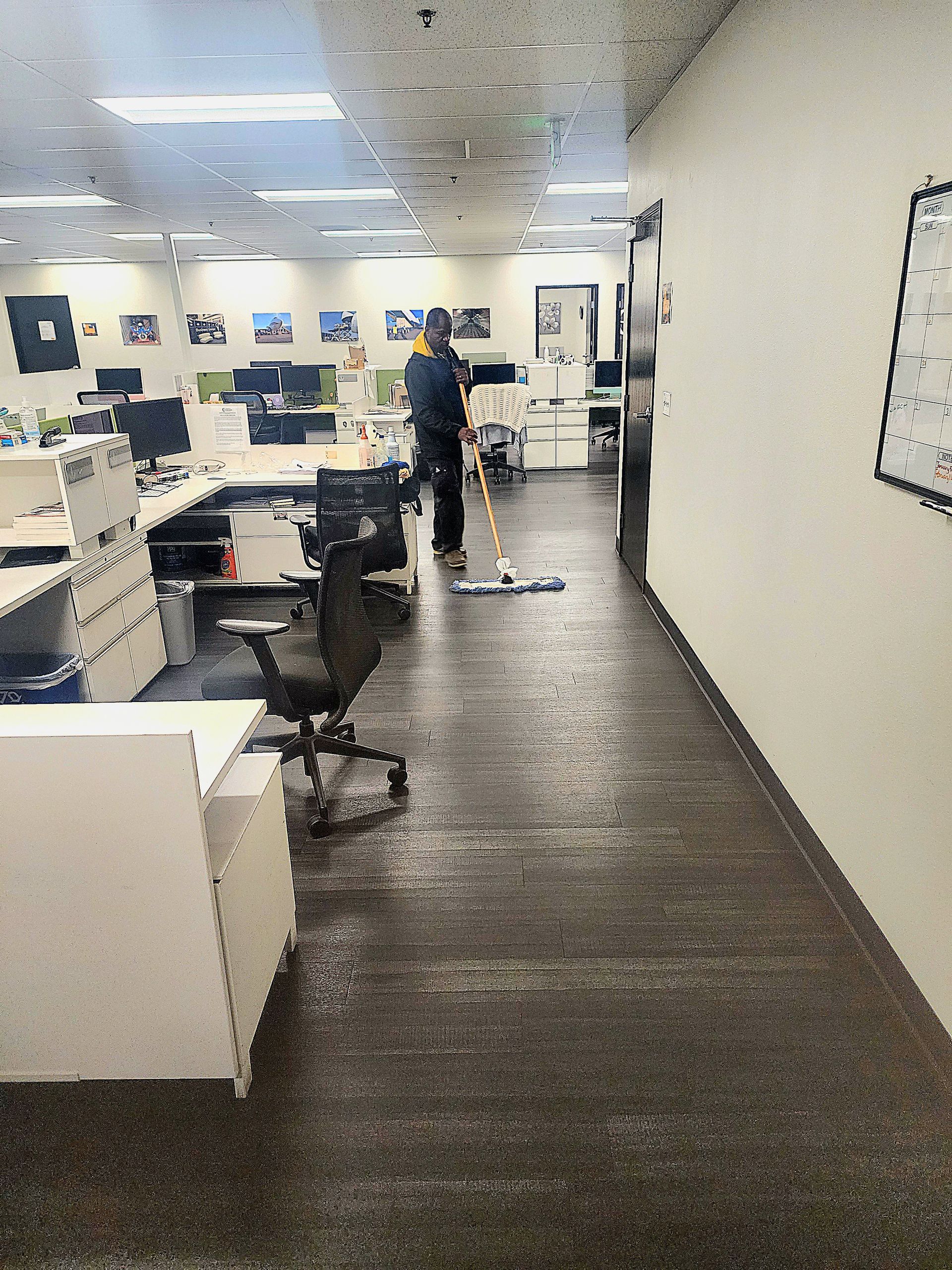 Office hallway with desks, office chairs, and a person standing near cubicles under bright fluorescent lights
