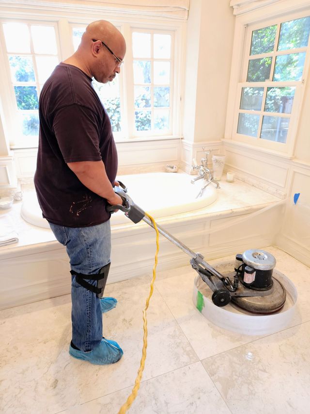Person using a floor buffer to polish a bright tiled bathroom floor near a bathtub.