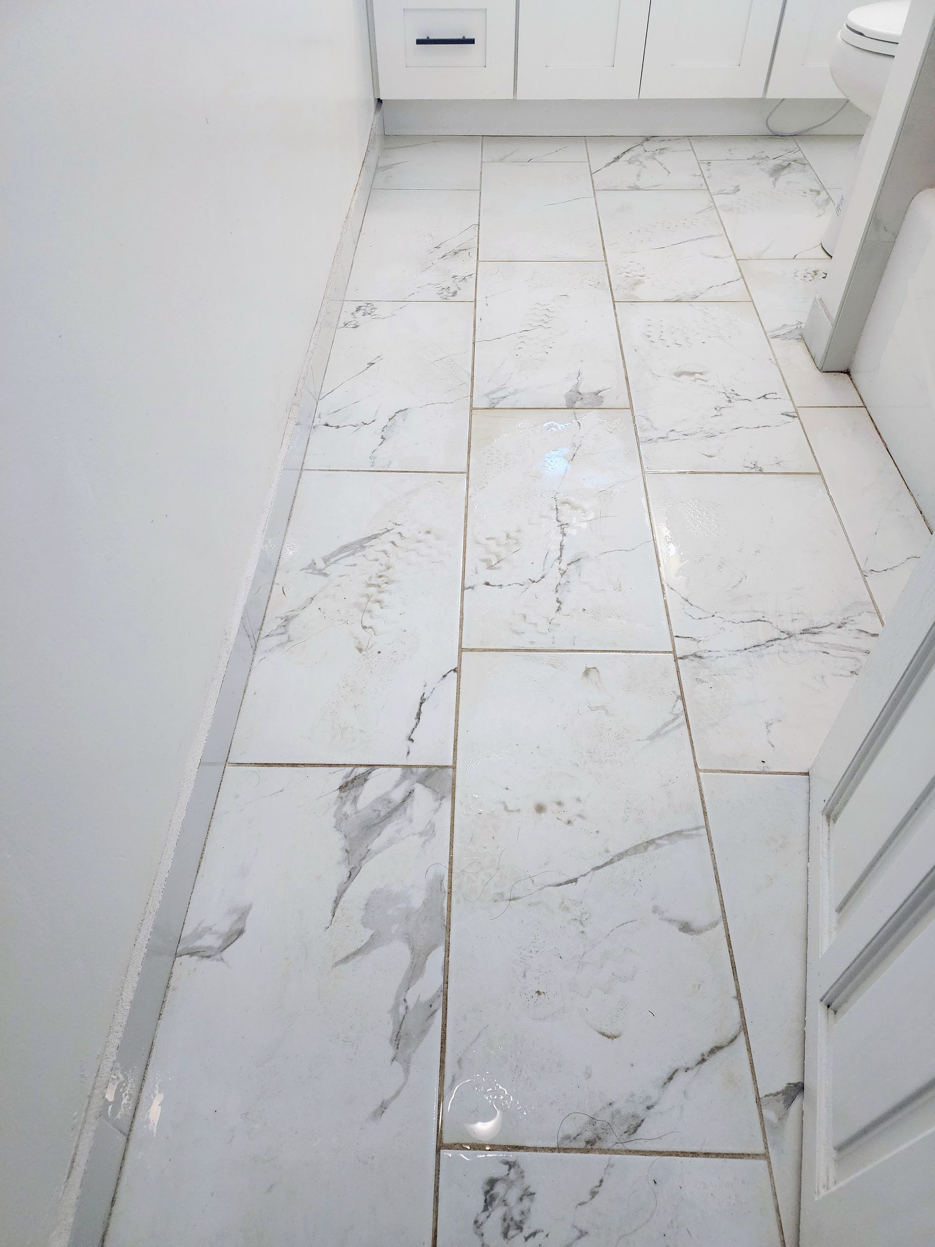 White marble-tile floor in a narrow hallway or bathroom with a cabinet and door trim.