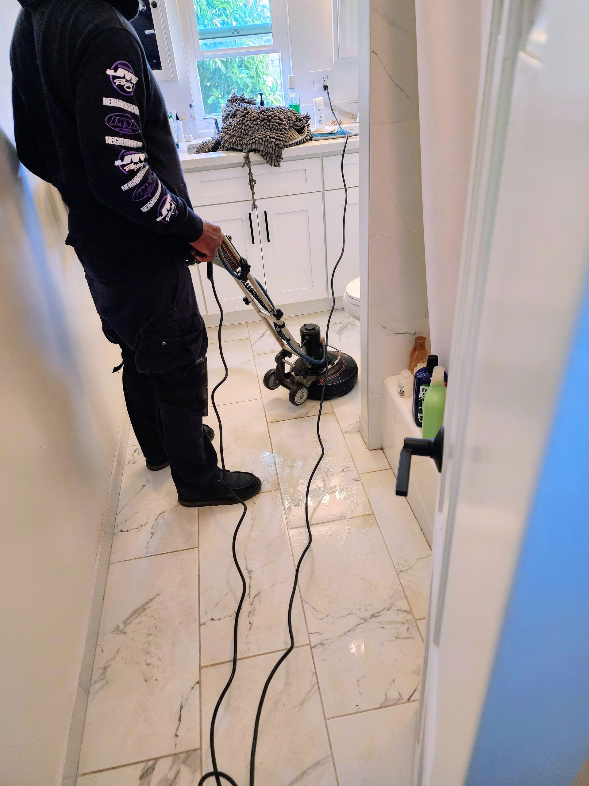 Person using a floor polisher on a tiled hallway floor with cords trailing behind.