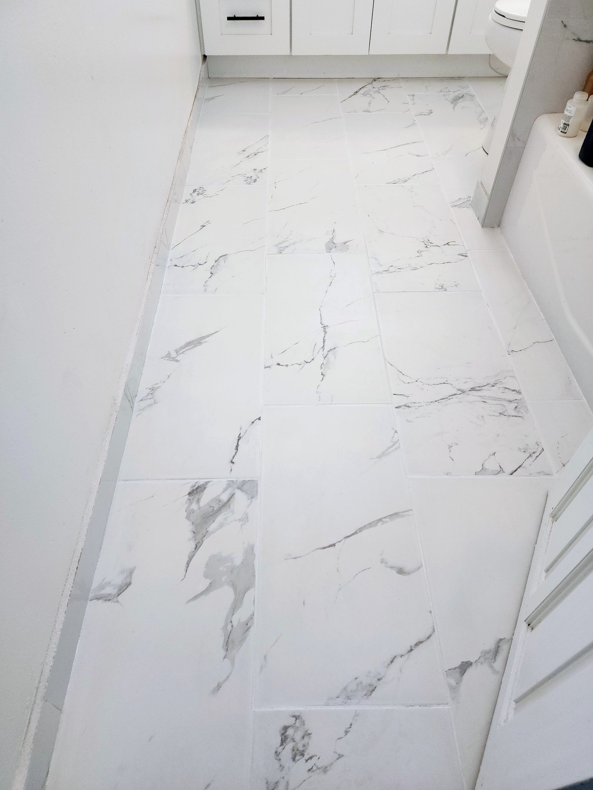 Narrow white hallway with marble-pattern tile floor and white cabinets at the end