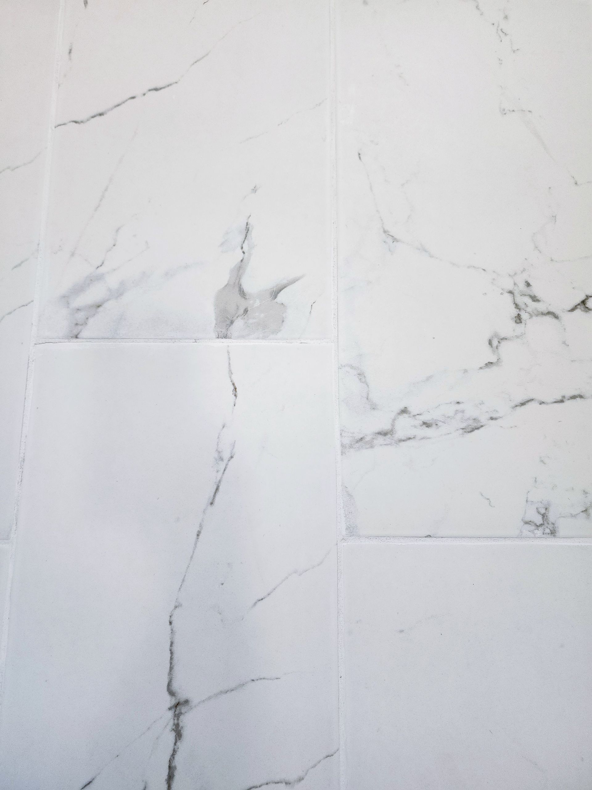 White marble wall tiles with gray veining and visible cracks and chips