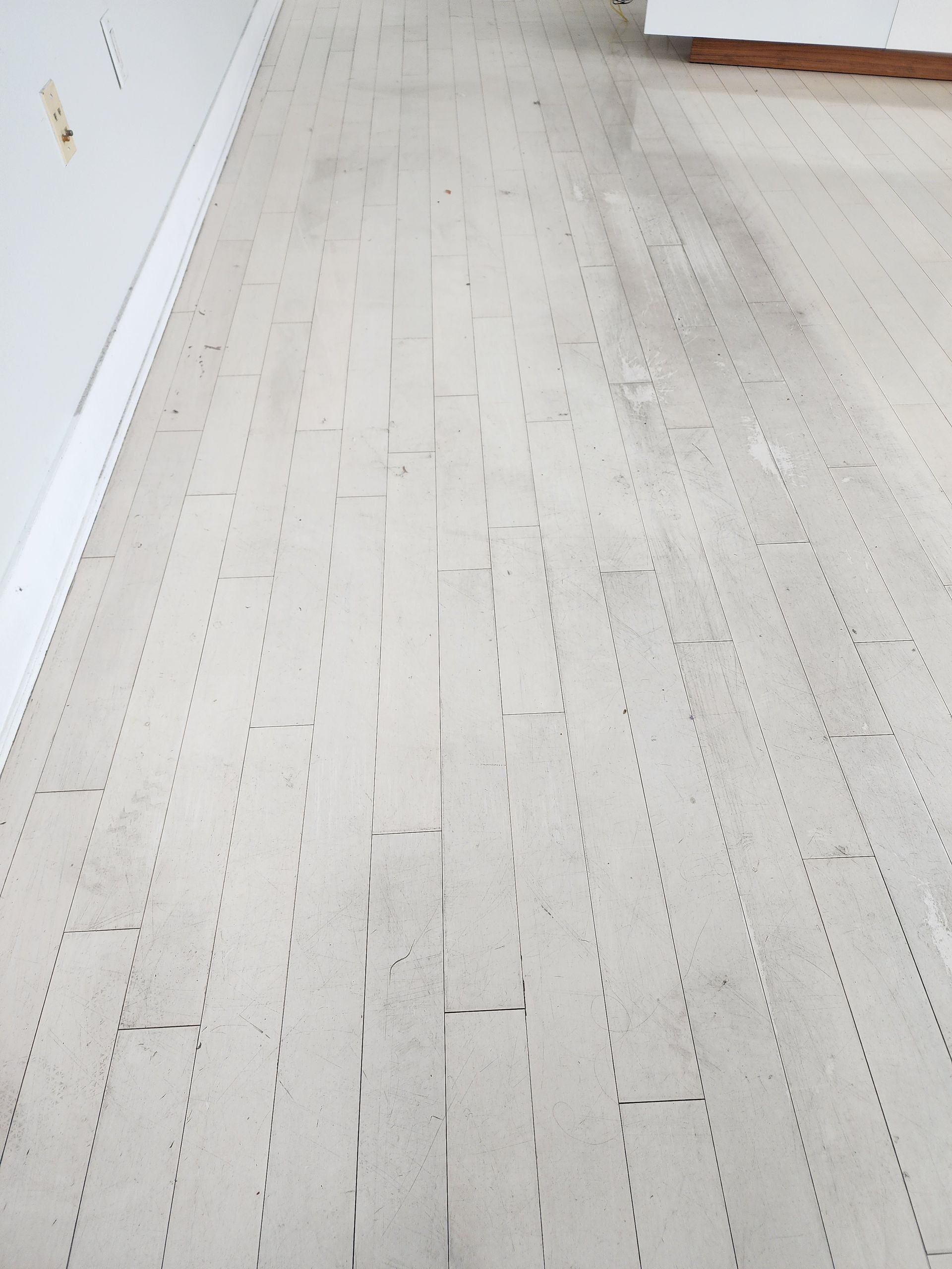 Light wood floor beside a white wall, with a wooden cabinet edge in the corner.
