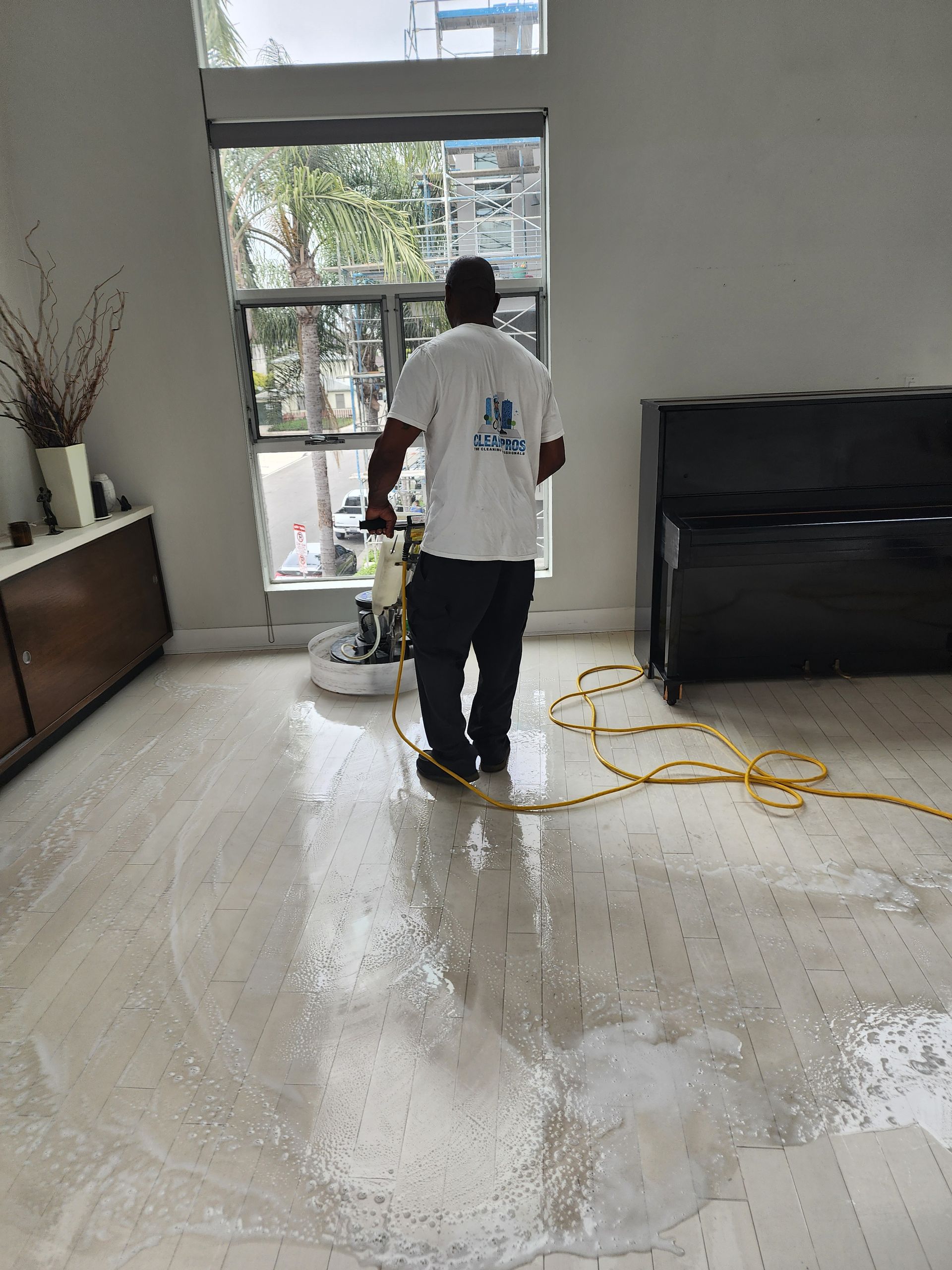 Person mopping a wet living room floor beside a yellow hose and TV.