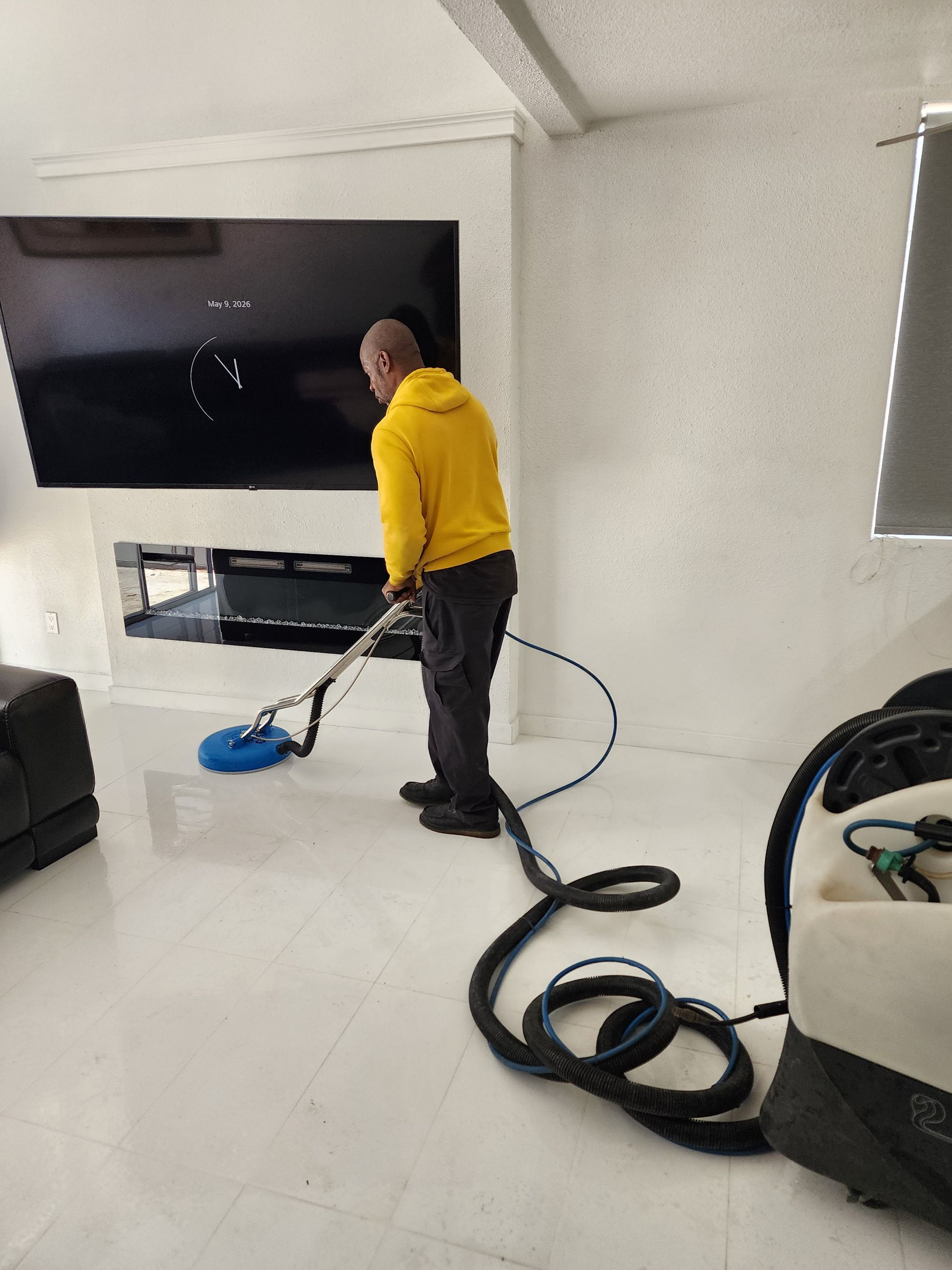 Person in a yellow shirt vacuuming a white living room with a black TV mounted on the wall