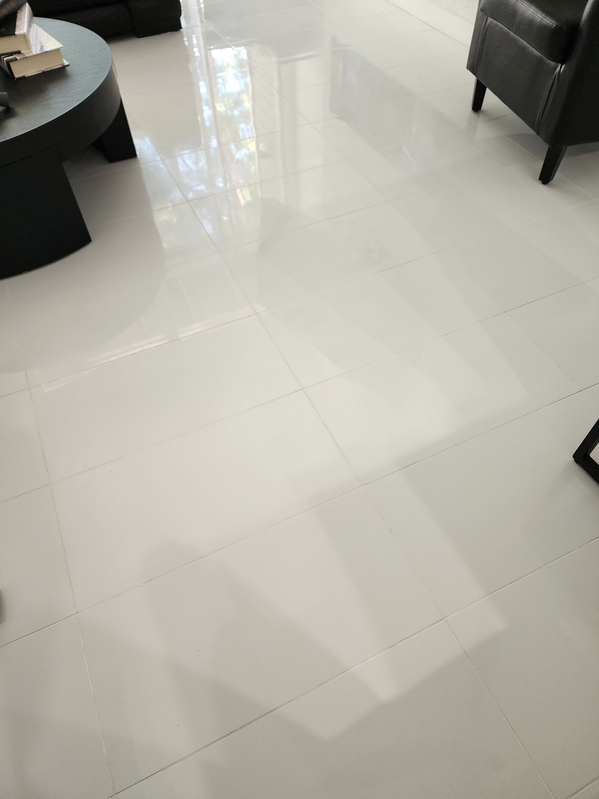 Bright white tiled floor in a modern room, with part of a dark table and chair visible.