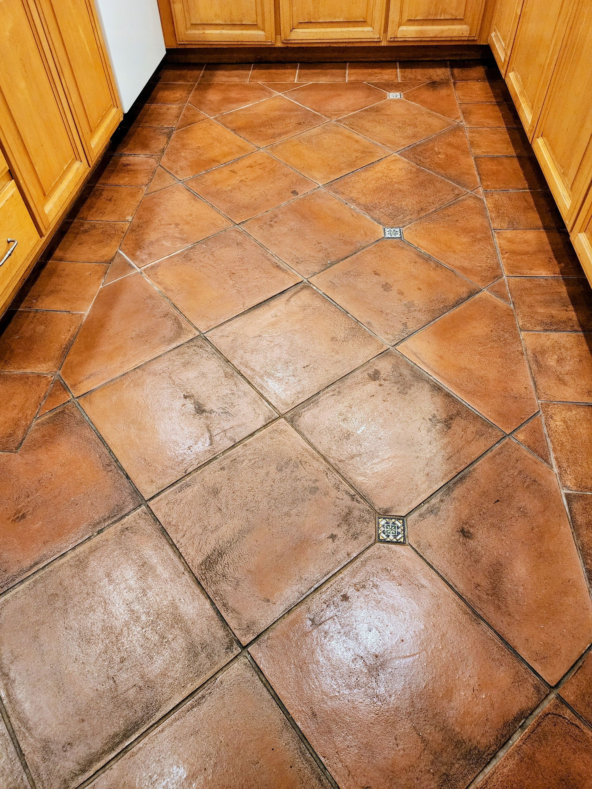 Terracotta tile floor with dark grout, viewed in a kitchen corner with wood cabinets.