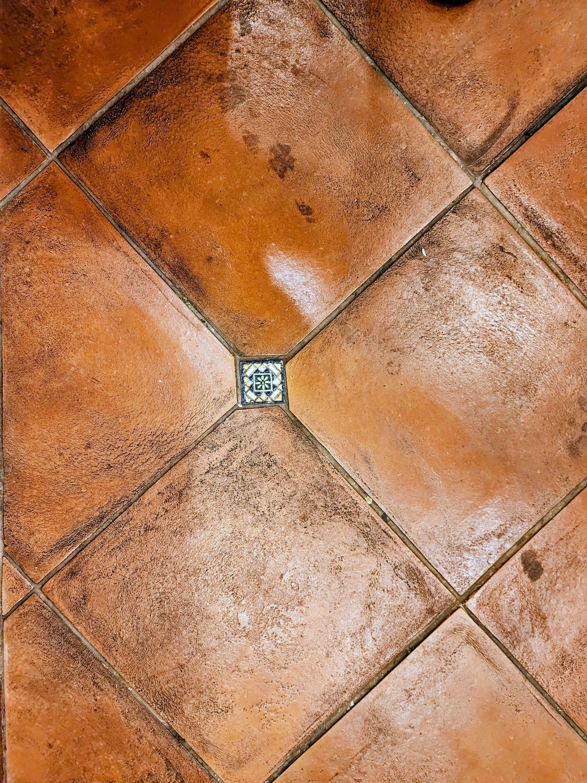 Orange-brown terracotta floor tiles with a small square mosaic at the center