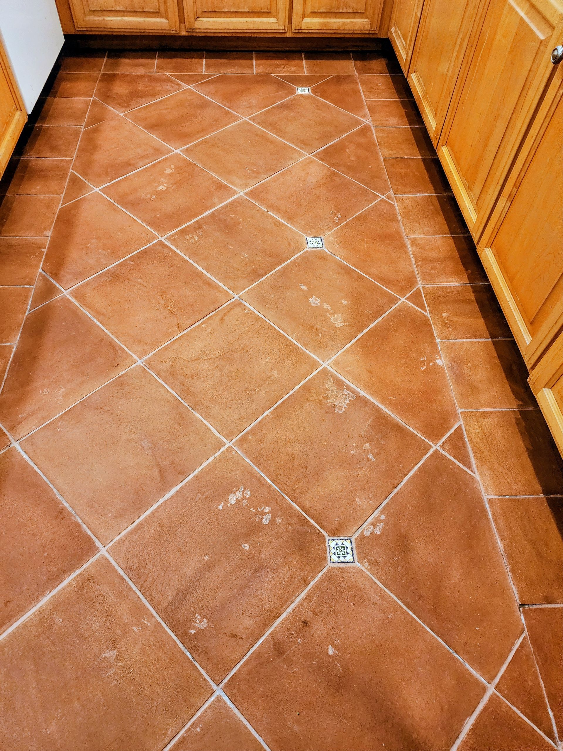 Terracotta tile kitchen floor with white grout lines and wooden cabinets along both sides
