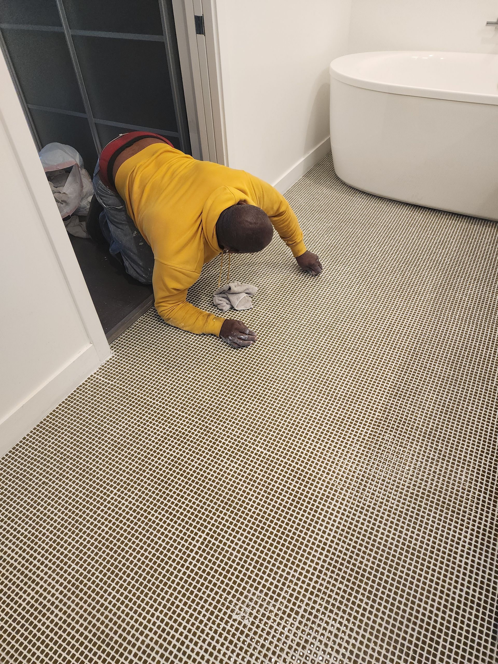 Person in a yellow hoodie crawling out of a closet onto a woven rug in a bathroom