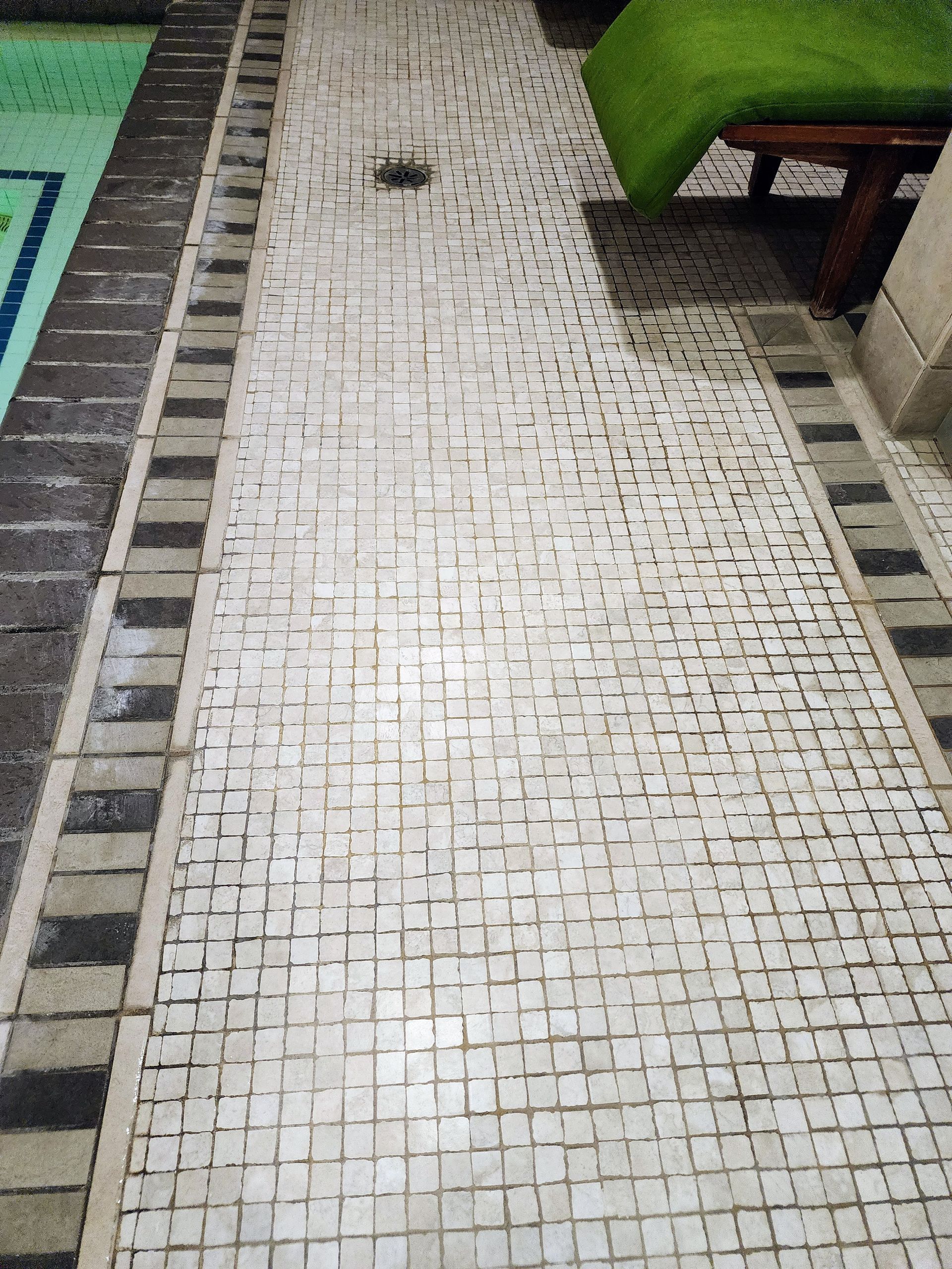 Narrow tiled walkway with a green bench and a dark hole in the path