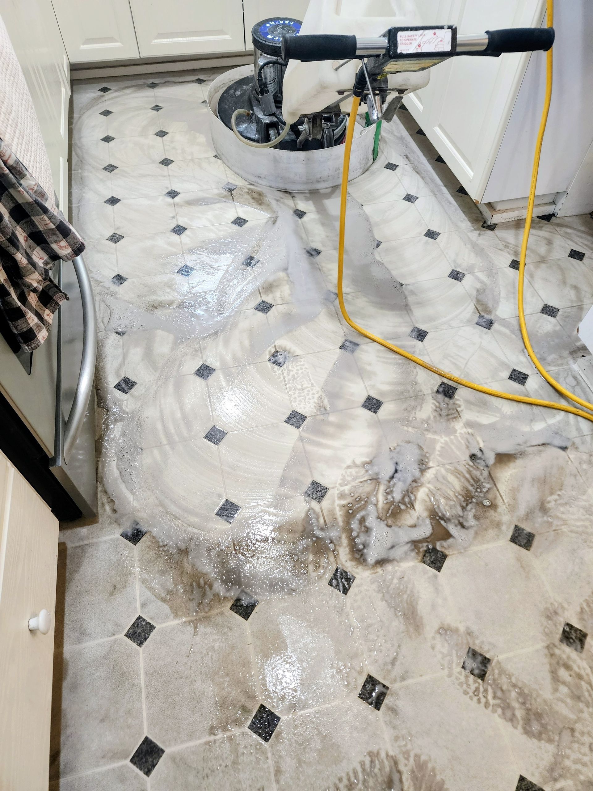 Bathroom floor being cleaned with a carpet extractor and yellow hose, water and grime visible on tile floor