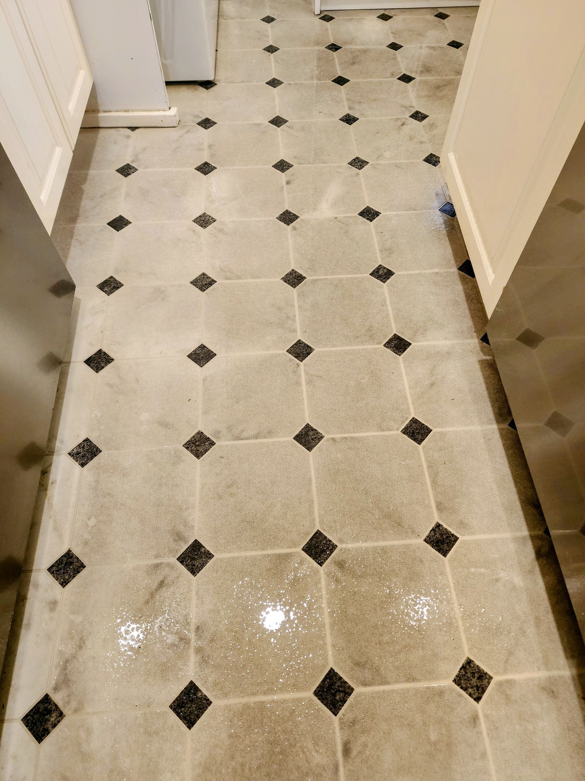 Man cleaning a tiled hallway with a floor machine and hoses in a hotel or apartment corridor