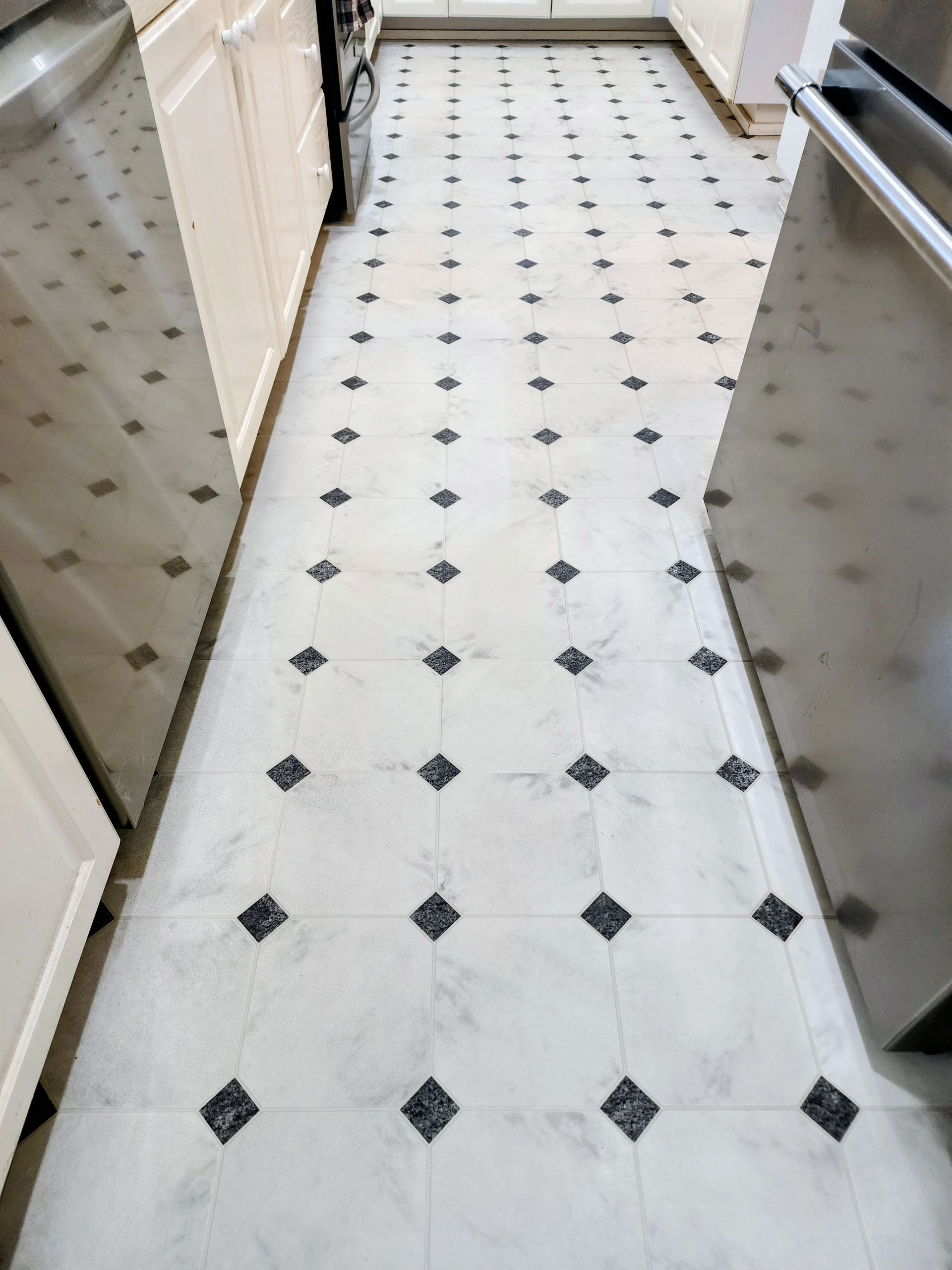 Narrow kitchen hallway with white tile floor and black diamond pattern, flanked by cabinets and walls