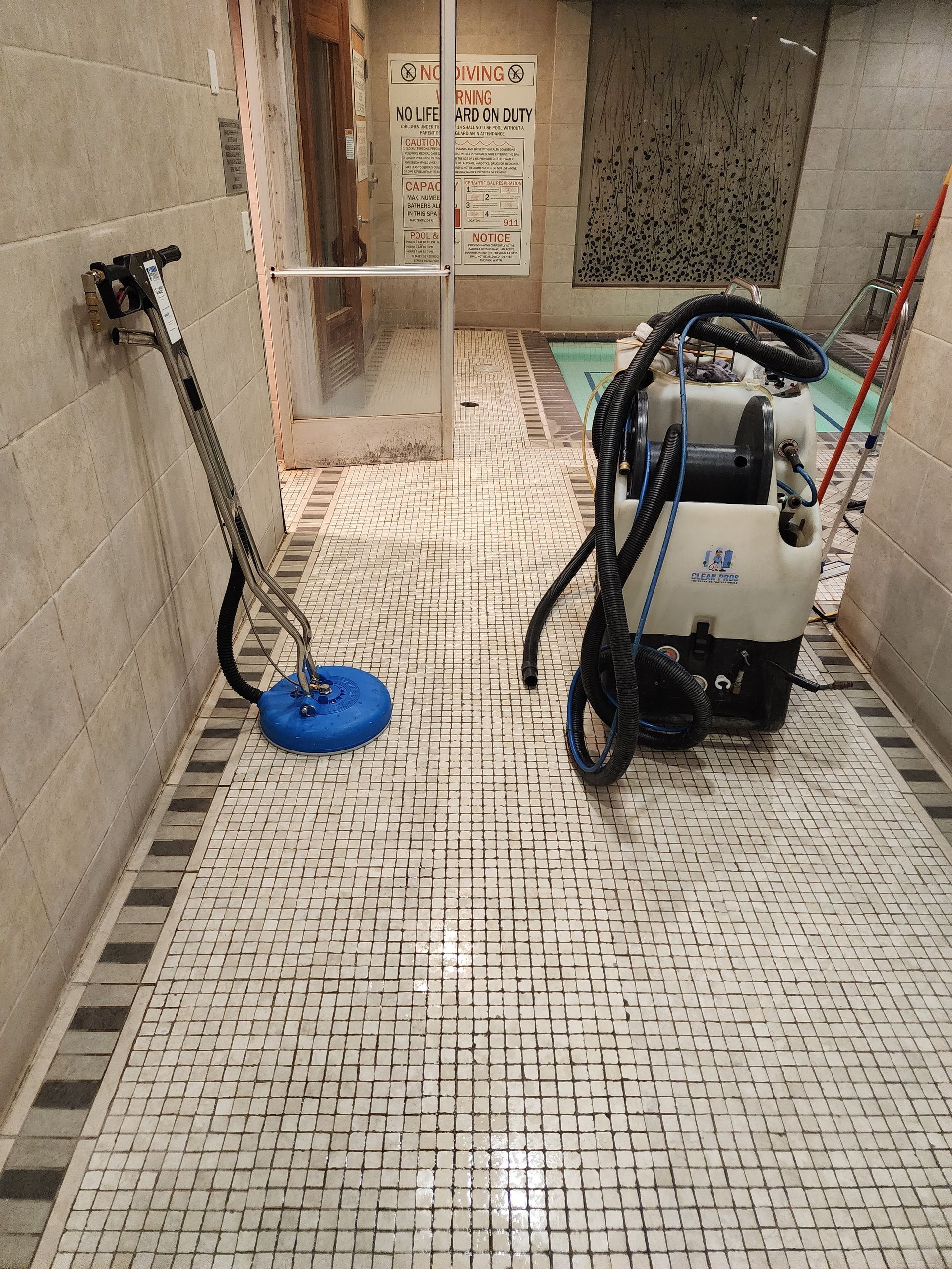 Mosaic-tiled hallway with cleaning equipment, including a floor scrubber and a blue floor buffer.