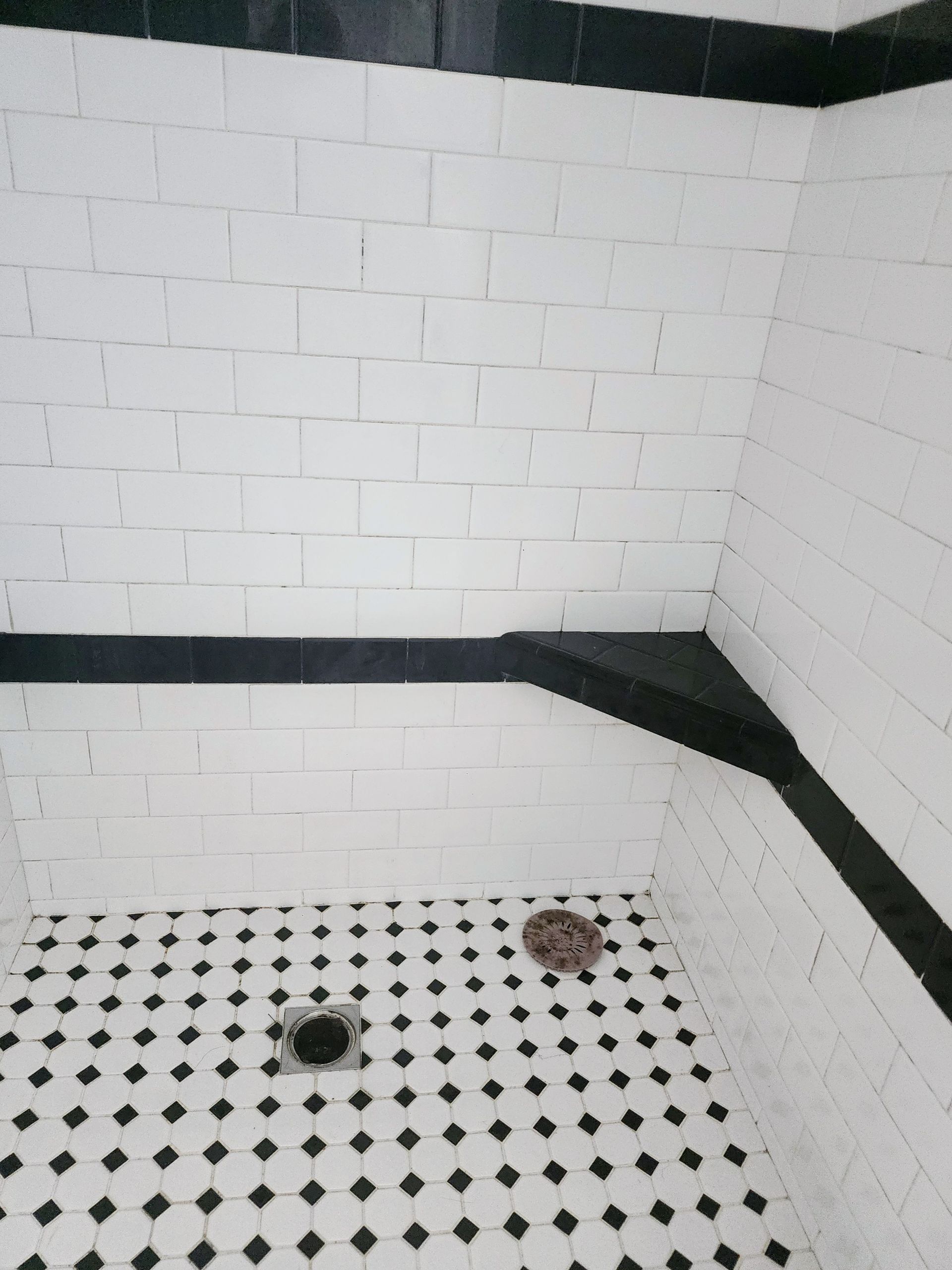 White tiled shower corner with black trim and two floor drains on a black-and-white diamond tile floor