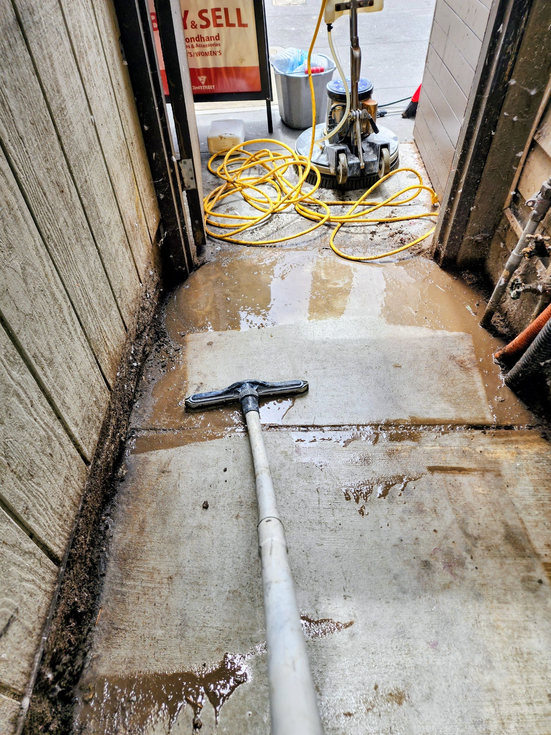Wet hallway with a mop on the floor and cleaning supplies near a doorway