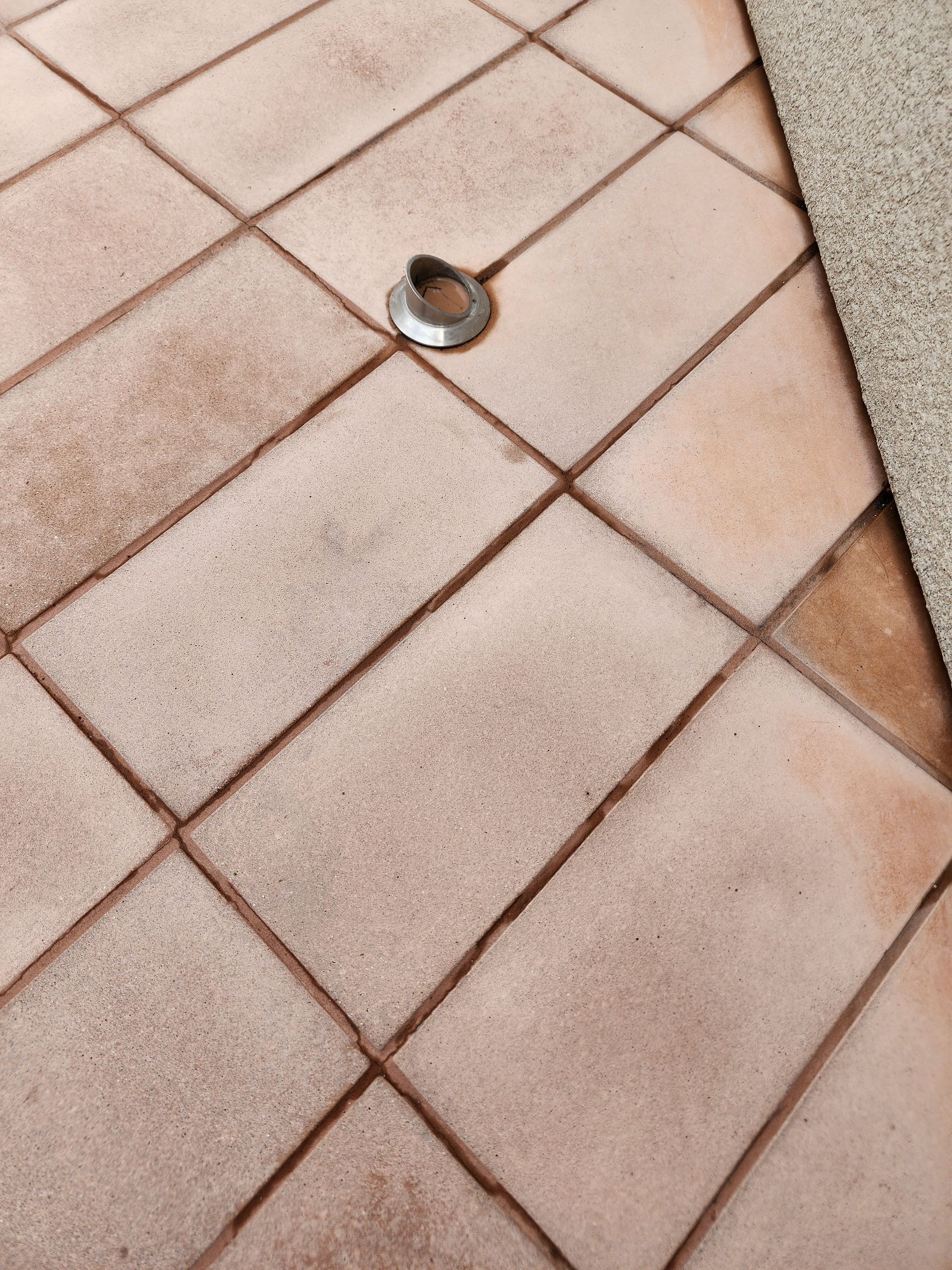 Small metal cap in a beige tiled floor, with a dark grout intersection nearby.