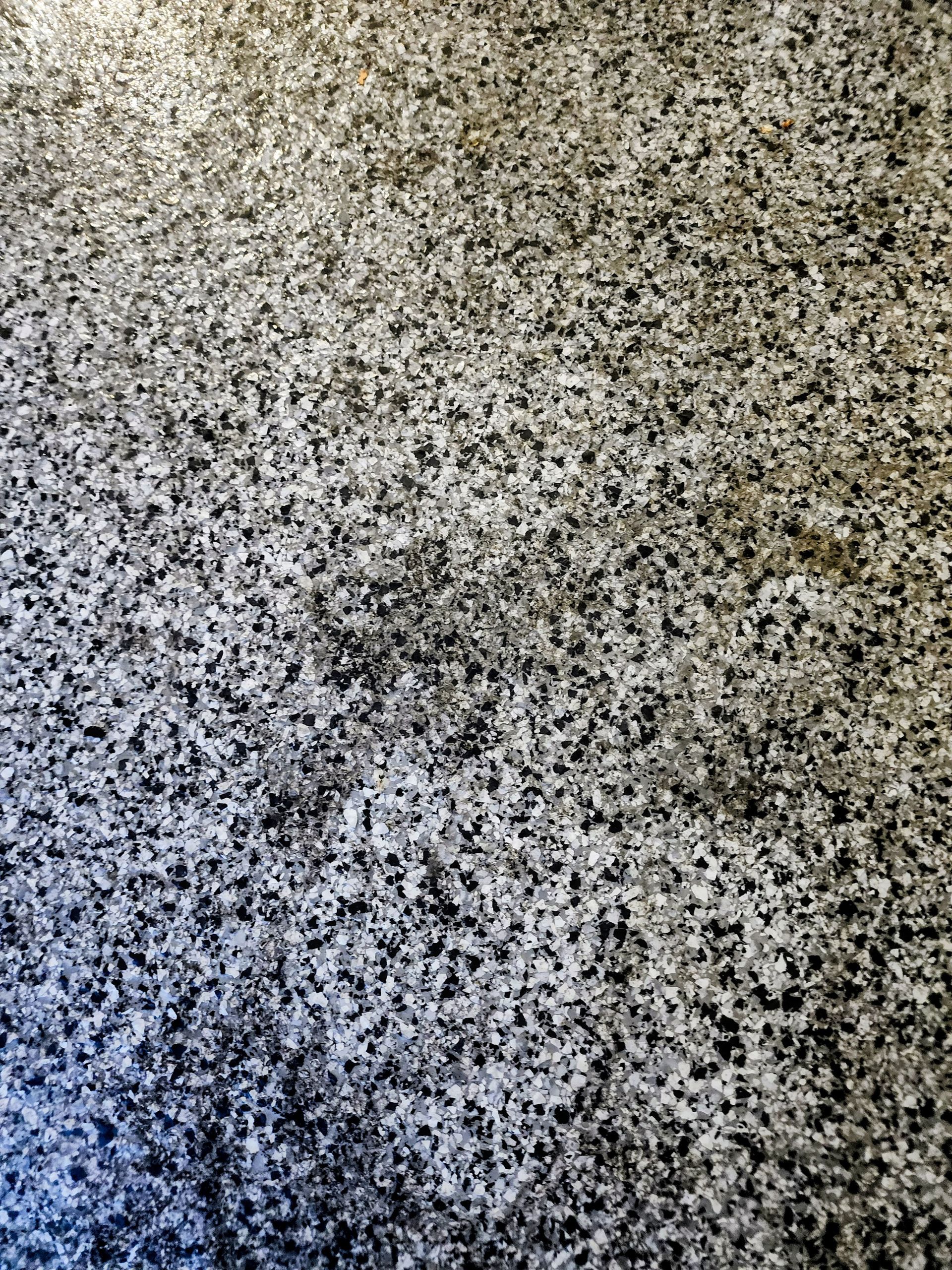 Close-up of speckled gray, black, and white stone or carpet texture with a bluish shadow in the lower left.