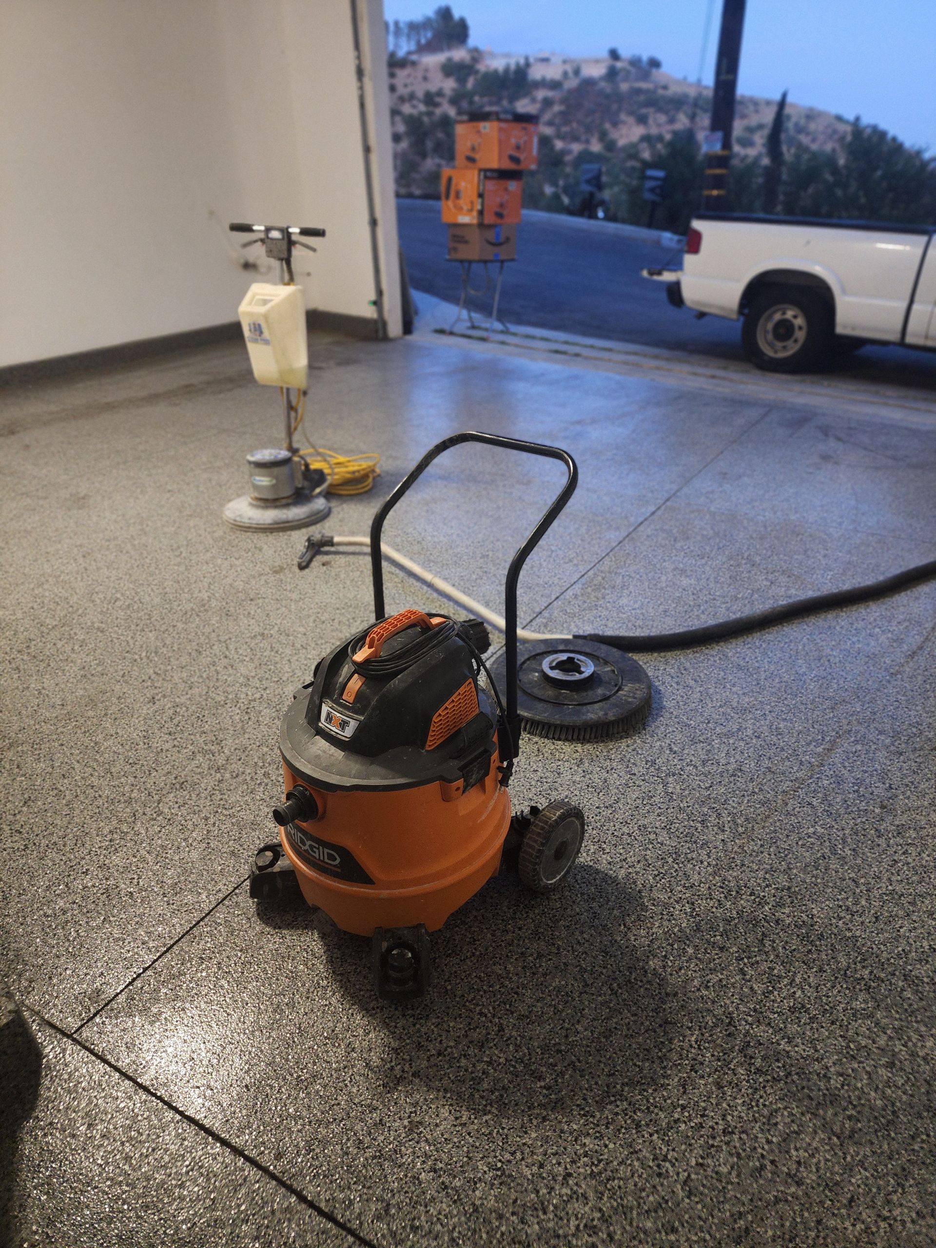 Orange wet/dry vacuum on a wet garage floor near an open doorway, with cleaning tools in the background