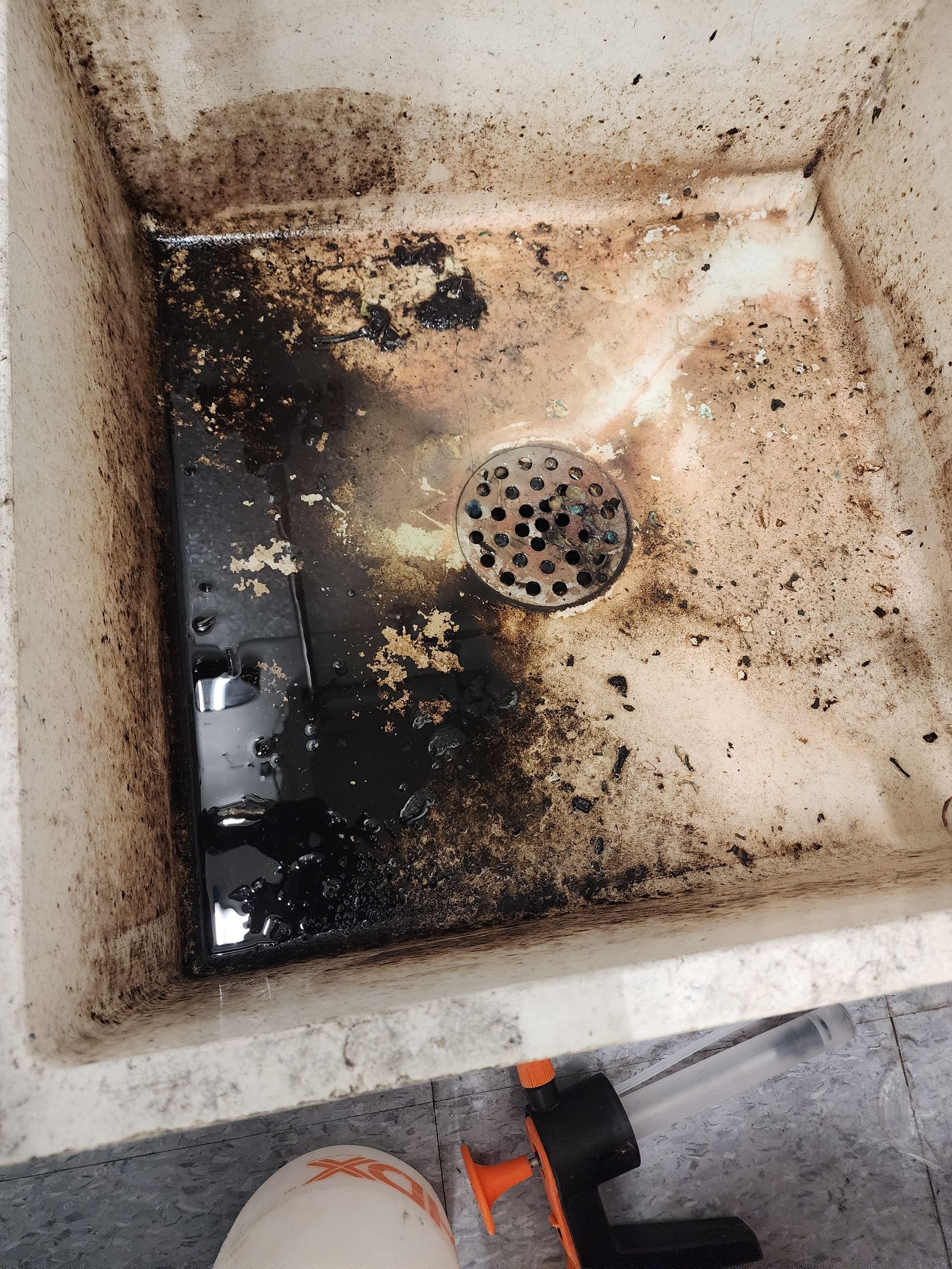 Dirty utility sink with black grime and a drain, viewed from above.