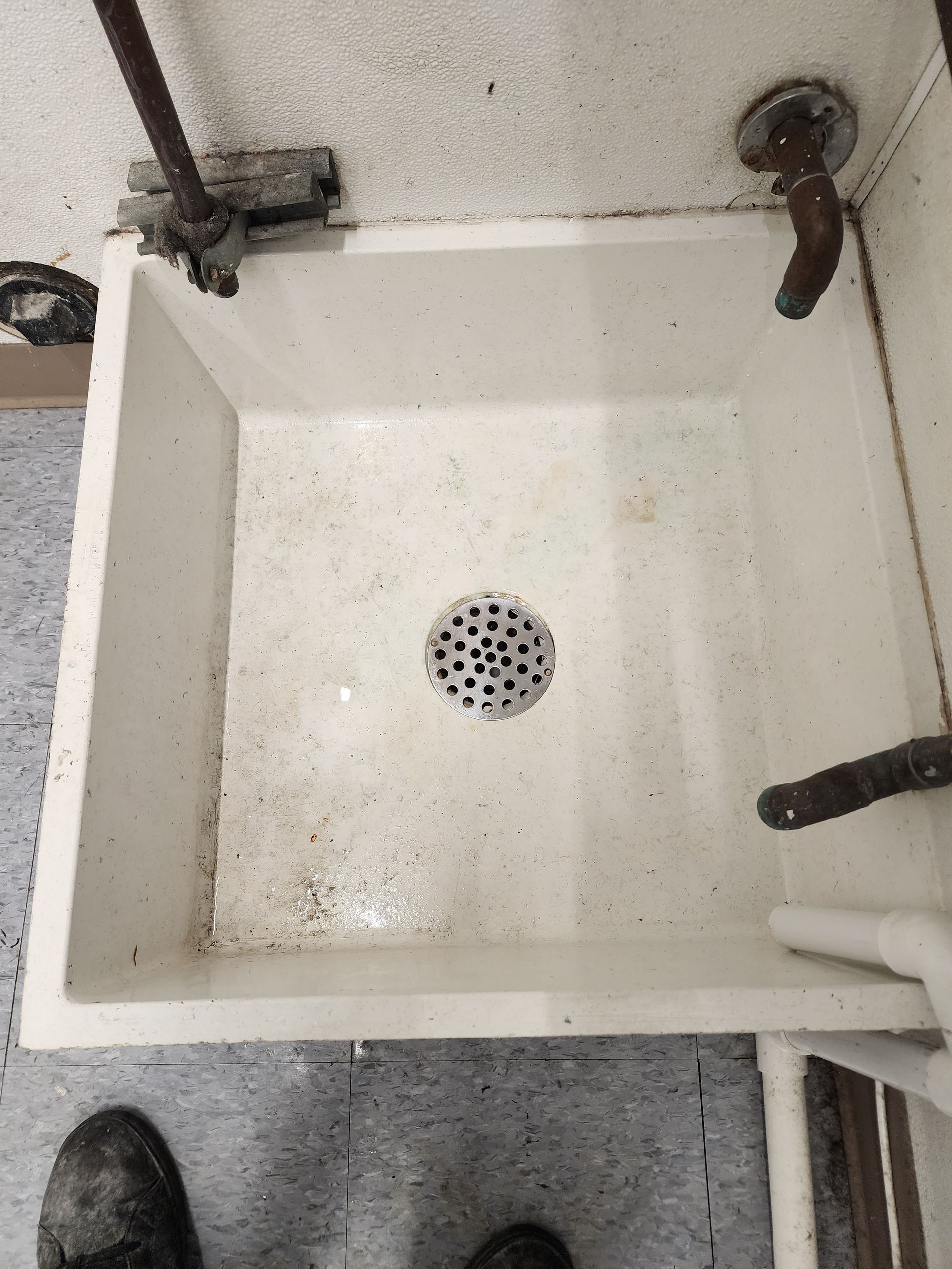 Dirty white utility sink with black grime and a drain visible.