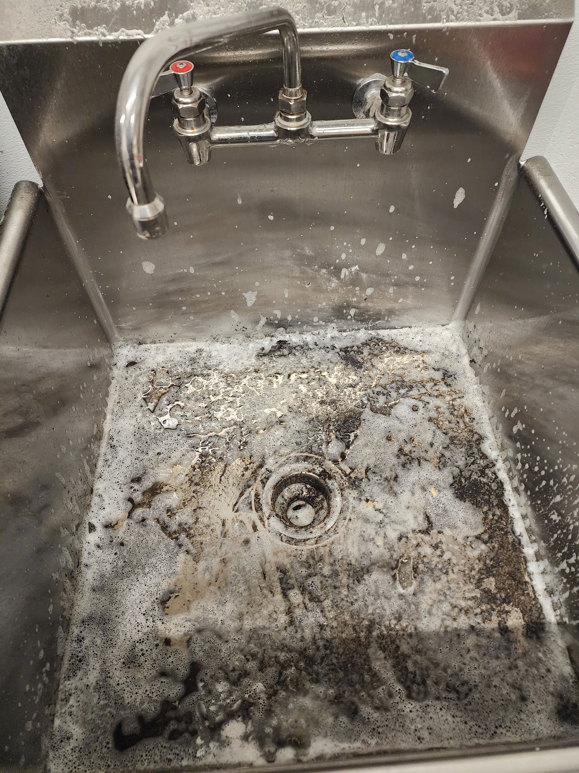 Dirty stainless steel sink with a stained basin and faucet above it