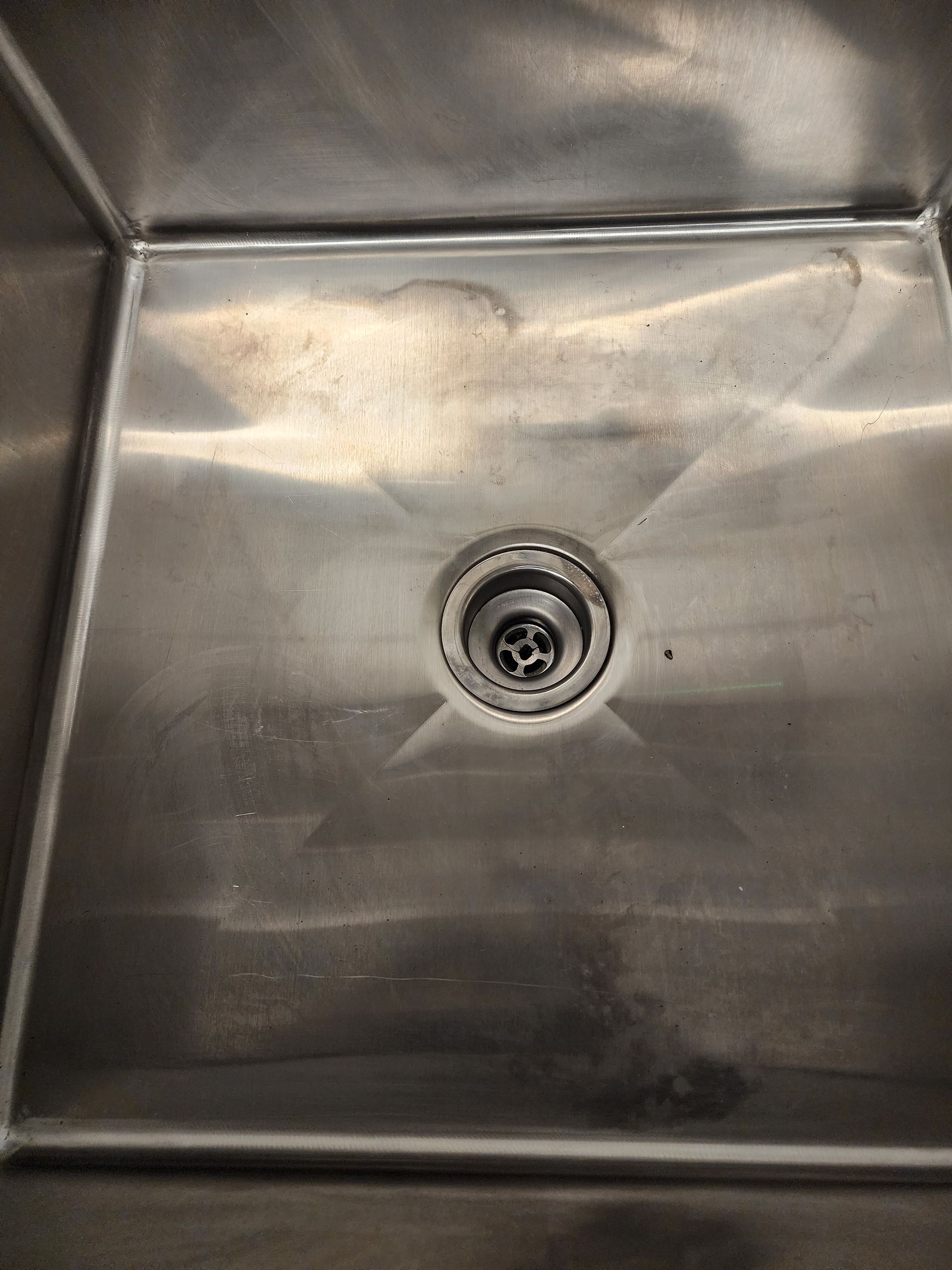 Stained white utility sink with drain and exposed pipes in a work area
