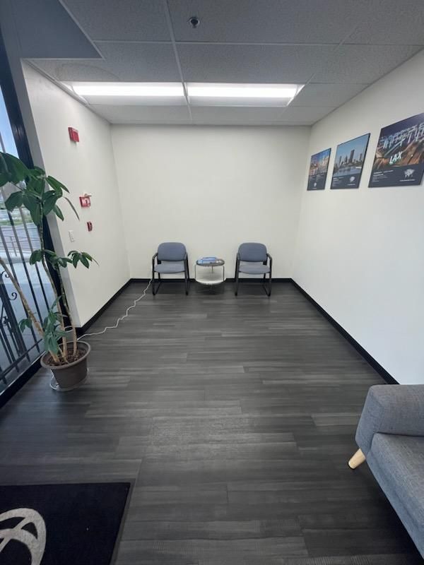 Small office waiting area with two chairs, a couch, a plant, and wall art on dark flooring.