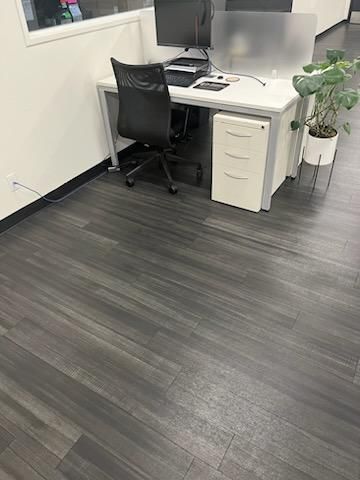 Modern office cubicle with desk, black chair, computer monitors, and potted plant on gray flooring