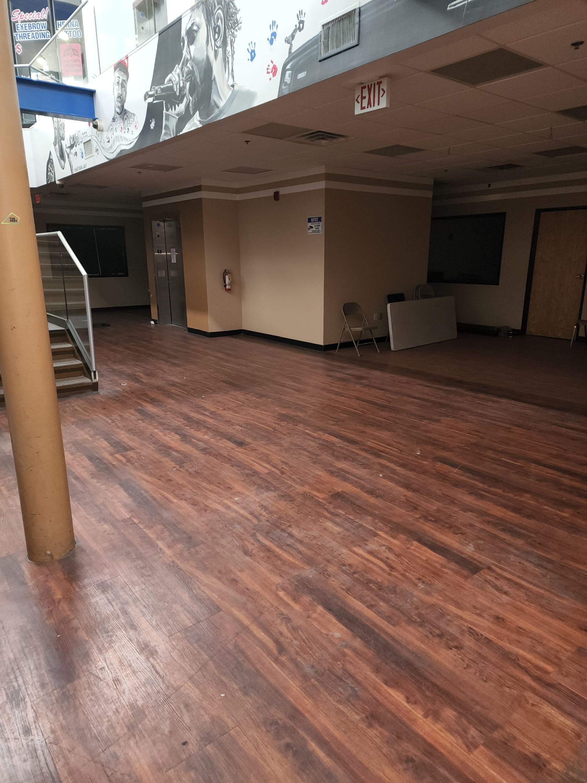 Empty indoor hall with wood-patterned floor, tan walls, and a low ceiling with damage above