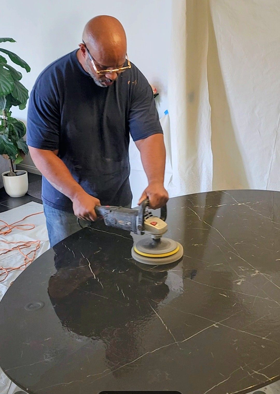 Person polishing a black marble tabletop with a power buffer in a bright room.