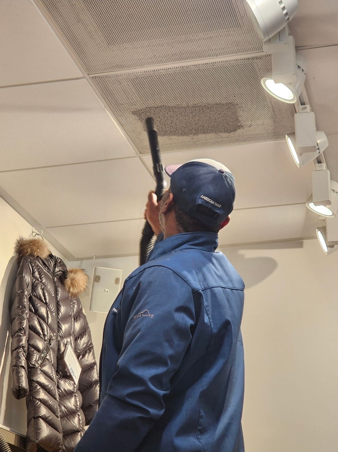 Person in a blue jacket using a handheld device to inspect the ceiling in a store.