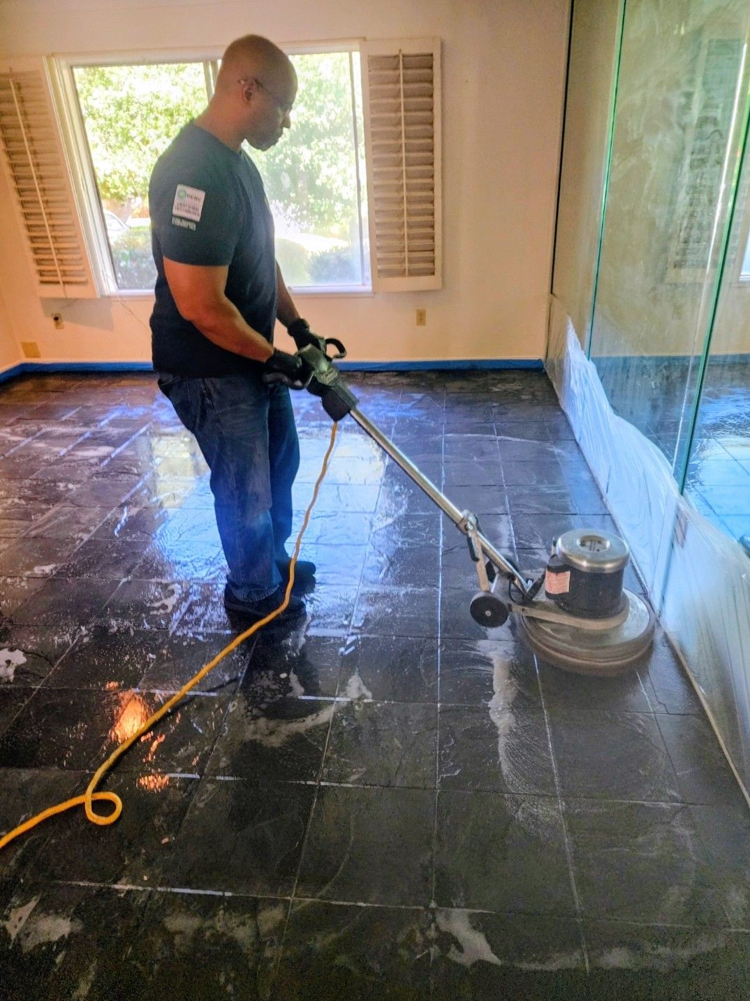 Worker cleaning a glossy black tile floor with a floor scrubber in a bright room