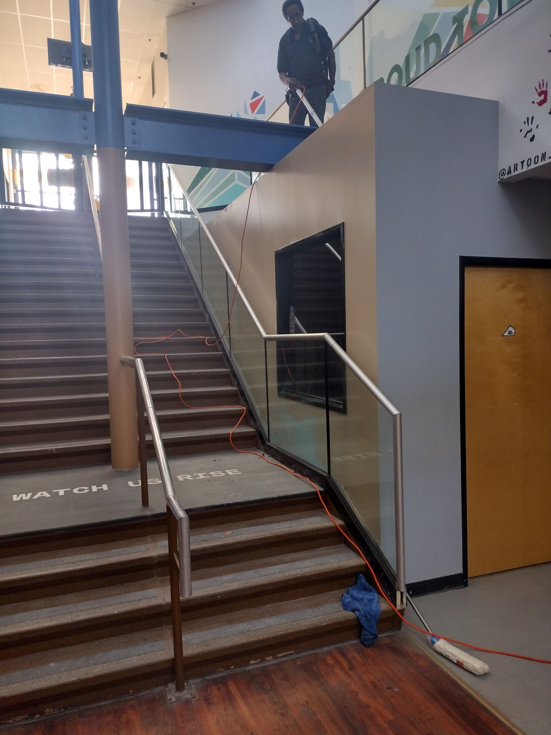 Interior stairwell with a central handrail, a person at the top landing, and a door beside the stairs