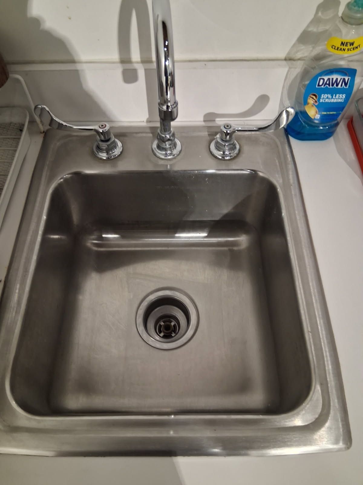 Stainless steel kitchen sink with chrome faucet and a blue dish soap bottle on the counter.