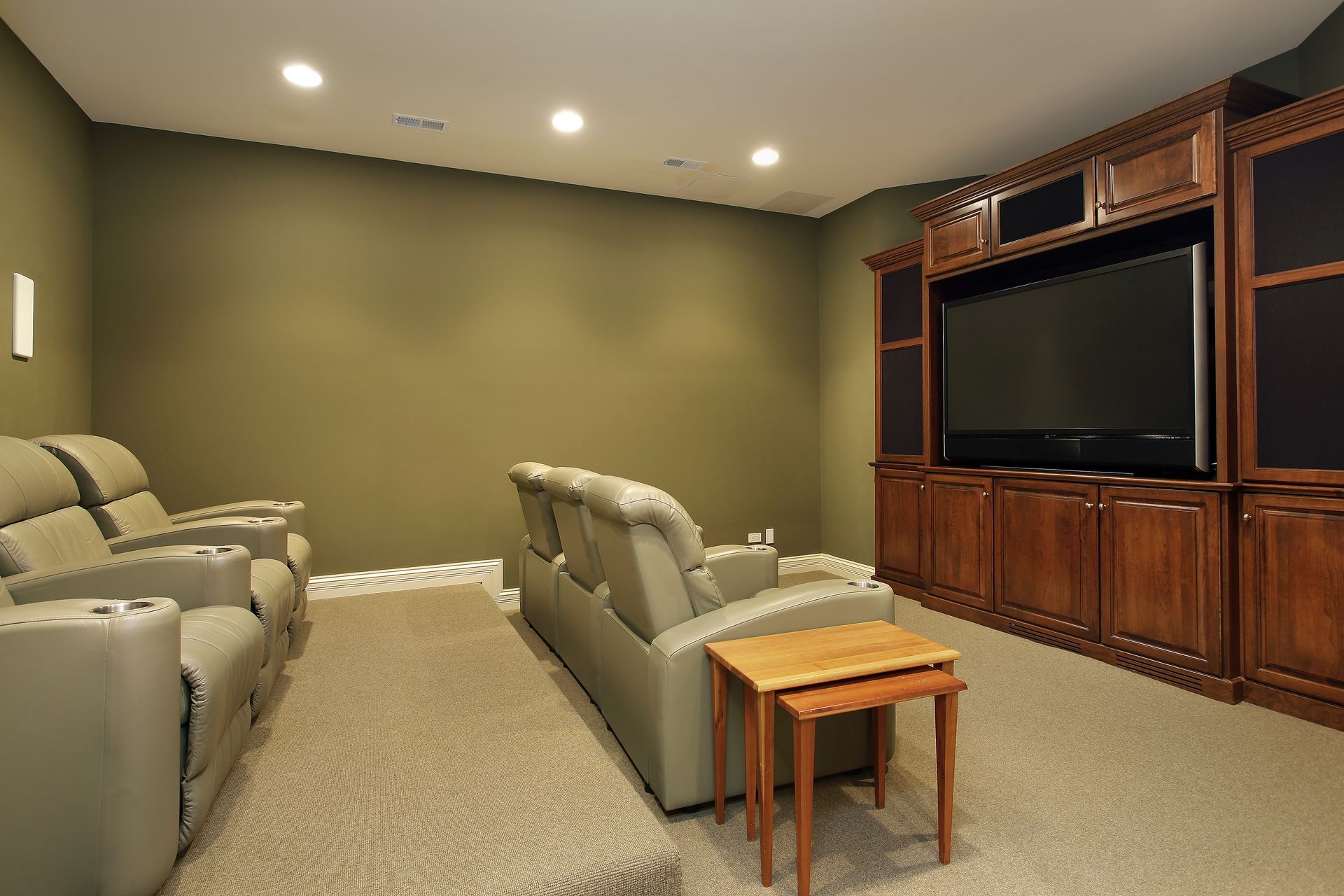 Home theater with two rows of grey leather reclining seats facing a large television in a wooden entertainment center.