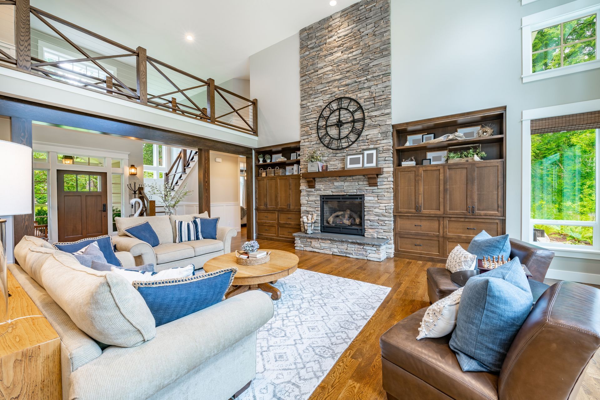 A spacious living room with a stone fireplace, built-in shelving, plush cream sofas with blue pillows, and a wooden loft.