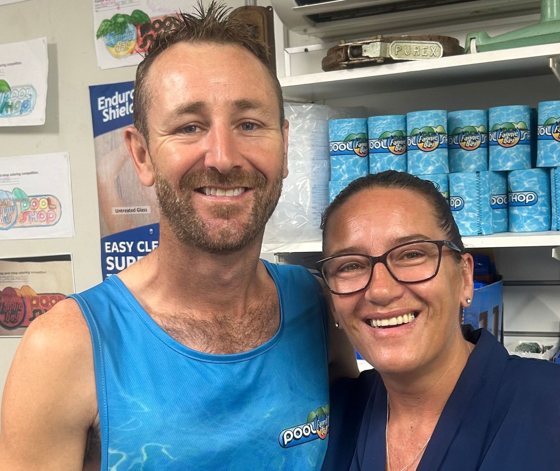 A Man And Women Smiling With Pool Supplies Behind Them — Fannie Bay Pool Shop in Winnellie, NT