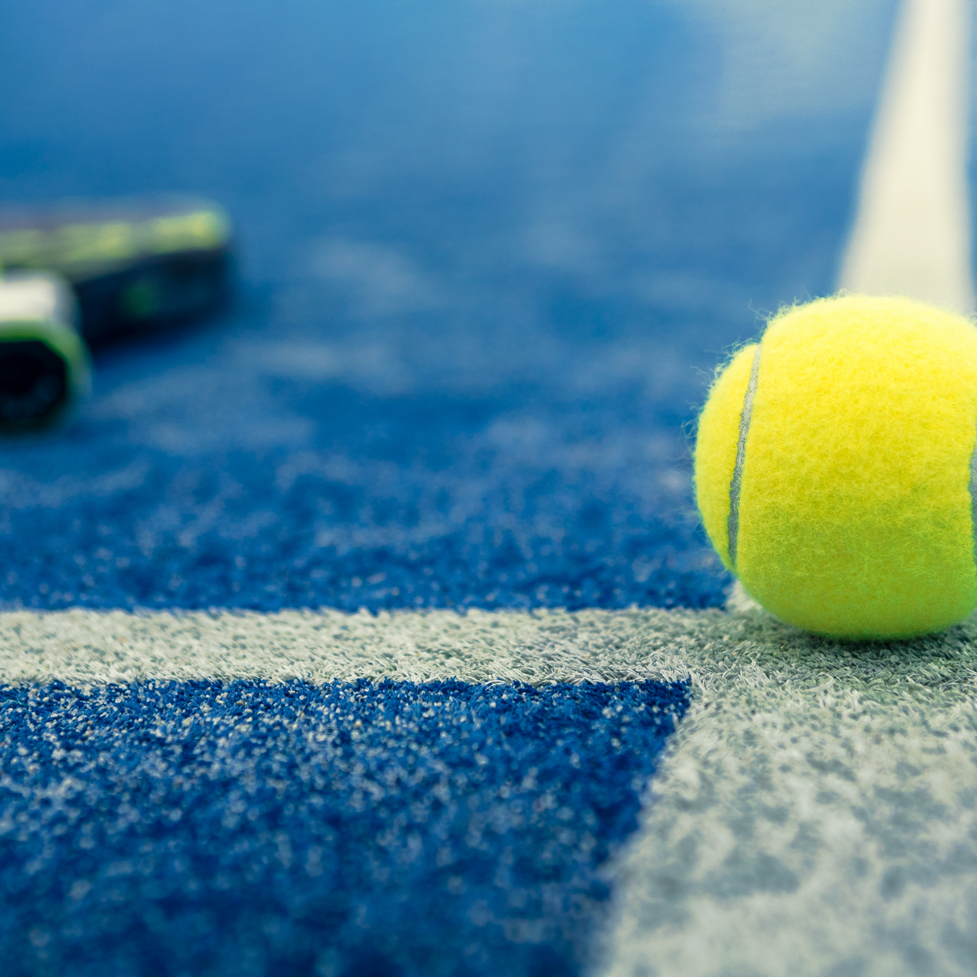 A tennis ball is sitting on the line of a tennis court.