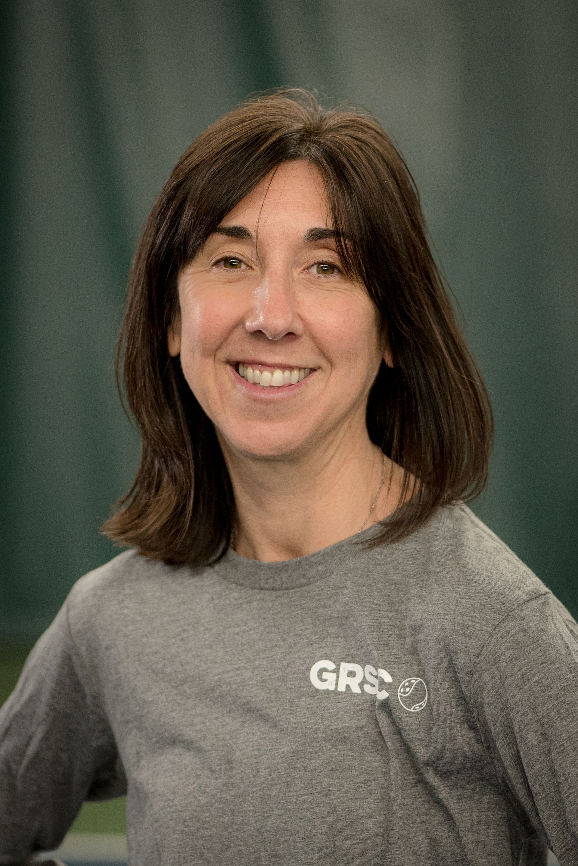A woman wearing a gray shirt is smiling for the camera.