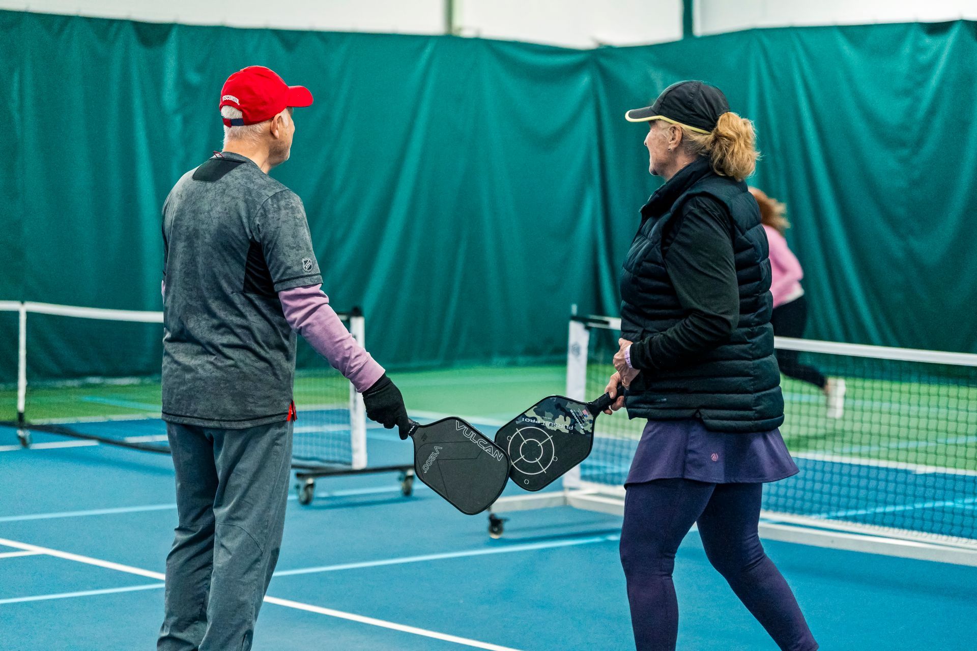 A man and a woman are playing pickleball on a tennis court.
