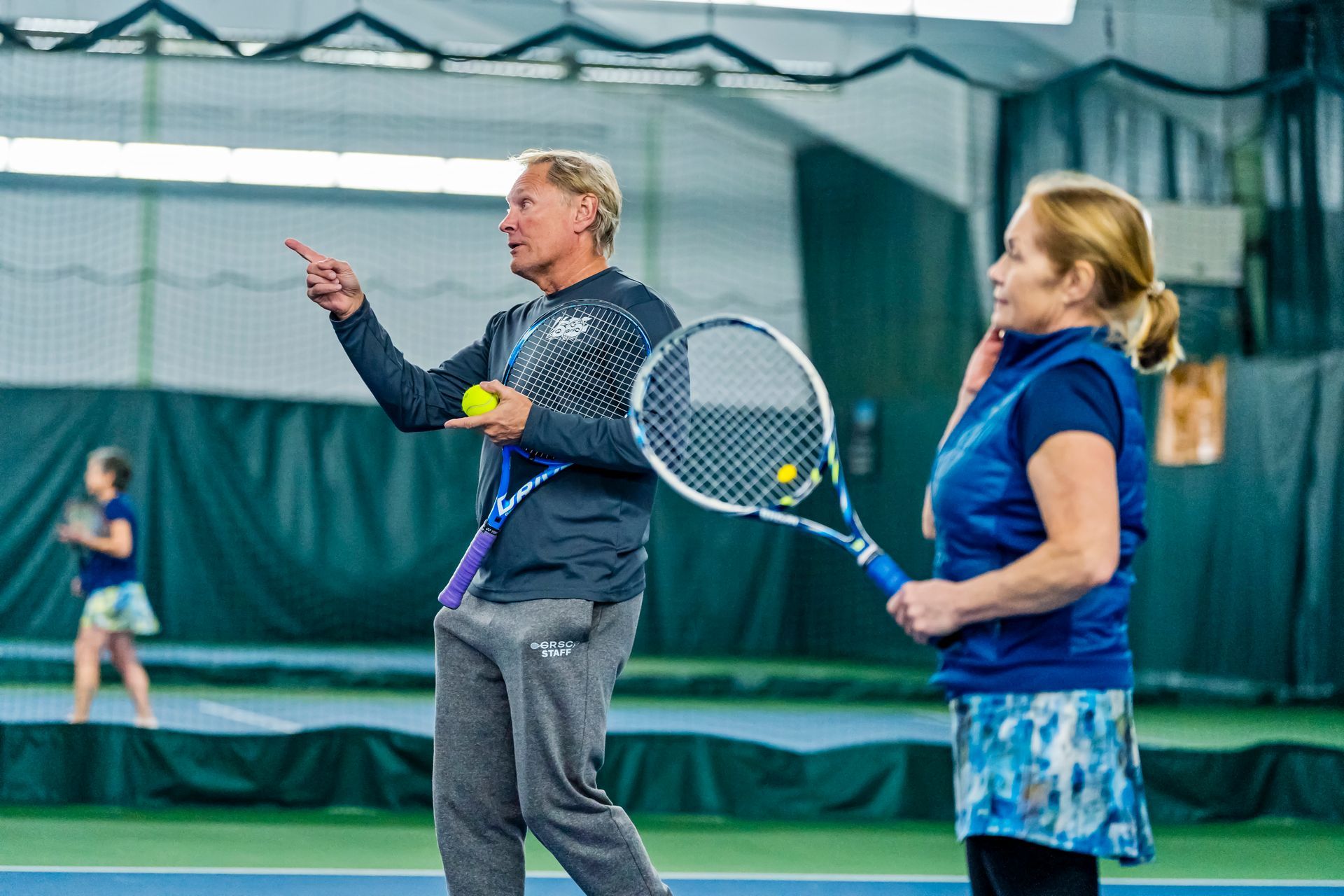 A man is teaching a woman how to play tennis on a tennis court.