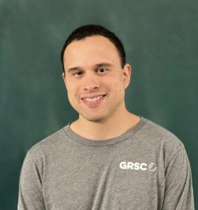 A man wearing a gray grsc shirt is smiling for the camera.