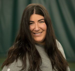 A woman wearing a gray shirt is smiling for the camera.