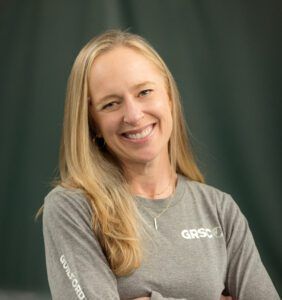 A woman wearing a gray shirt is smiling with her arms crossed.